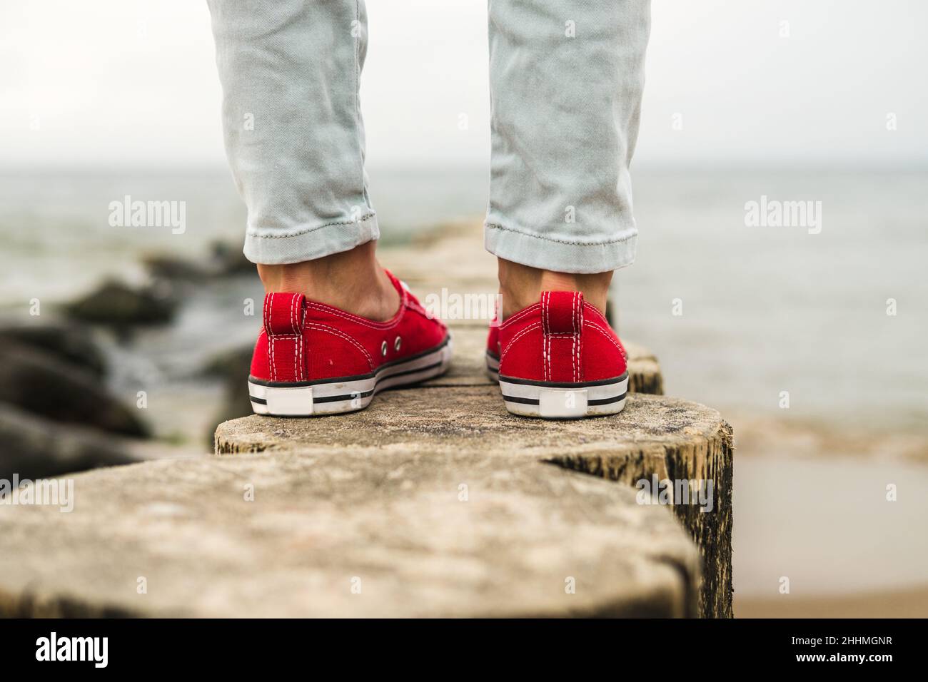 Damenbeine in roten Sneakers und Jeans am Meer. Reisekonzept. Stockfoto
