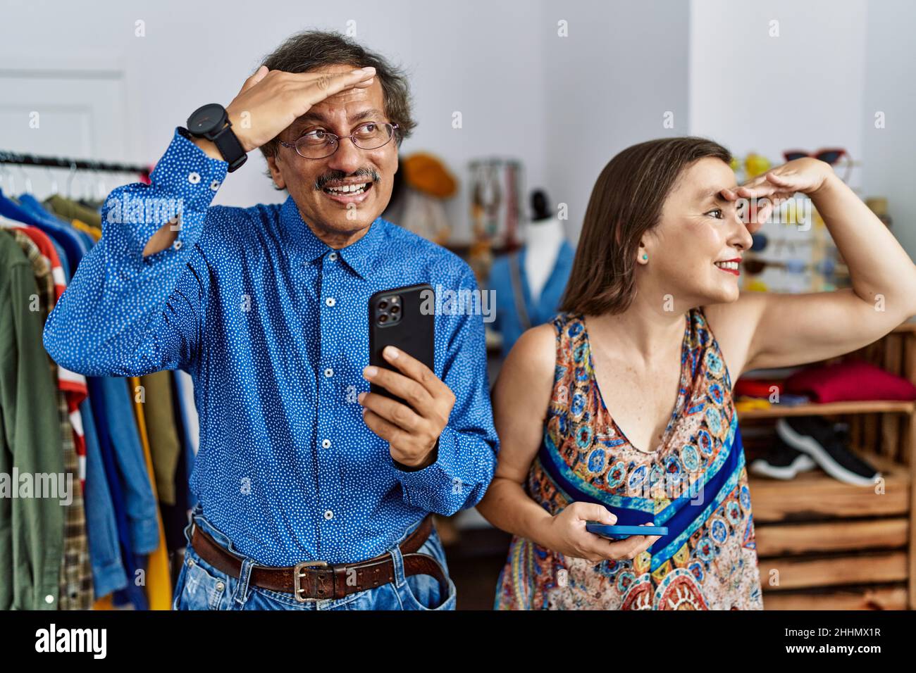 Interrassisches Paar im mittleren Alter im Einzelhandel mit Smartphone sehr glücklich und lächelnd, weit weg mit der Hand über dem Kopf. Suchkonzept. Stockfoto
