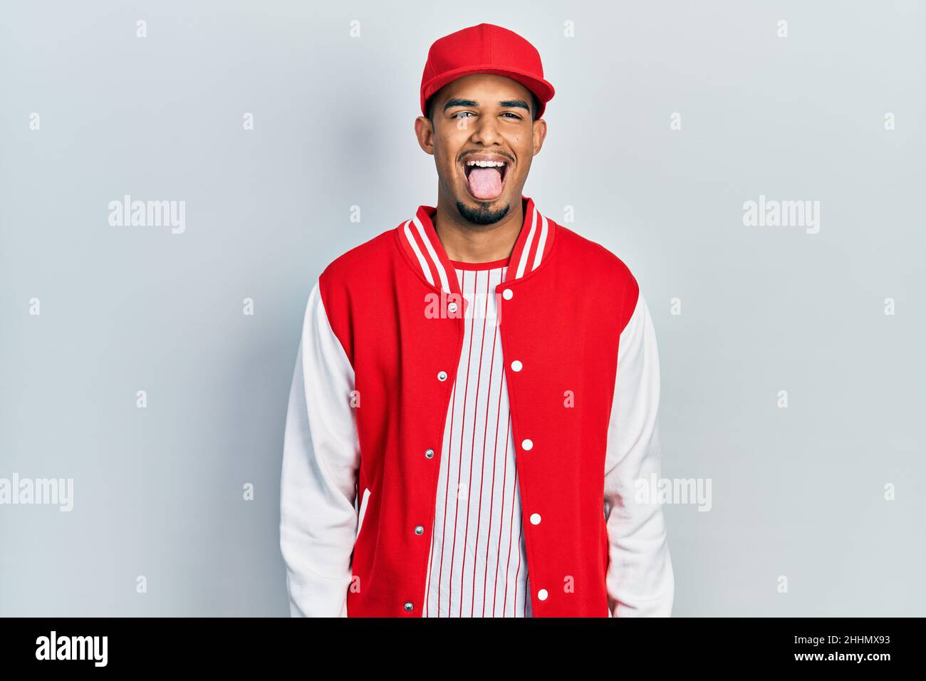 Junger afroamerikanischer Mann mit Baseballuniform, der die Zunge herausstreckt, glücklich mit einem lustigen Ausdruck. Emotionskonzept. Stockfoto