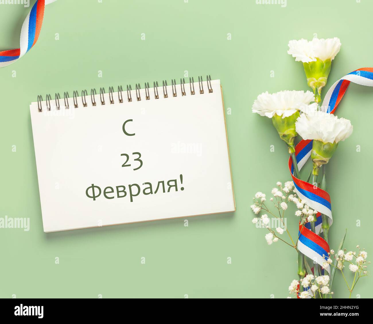 Herrentag-Glückwunschkarte mit weißen Nelken und Gypsophila mit russischem Flaggenband auf grünem Hintergrund mit Inschrift am 23. Februar. Männer Stockfoto