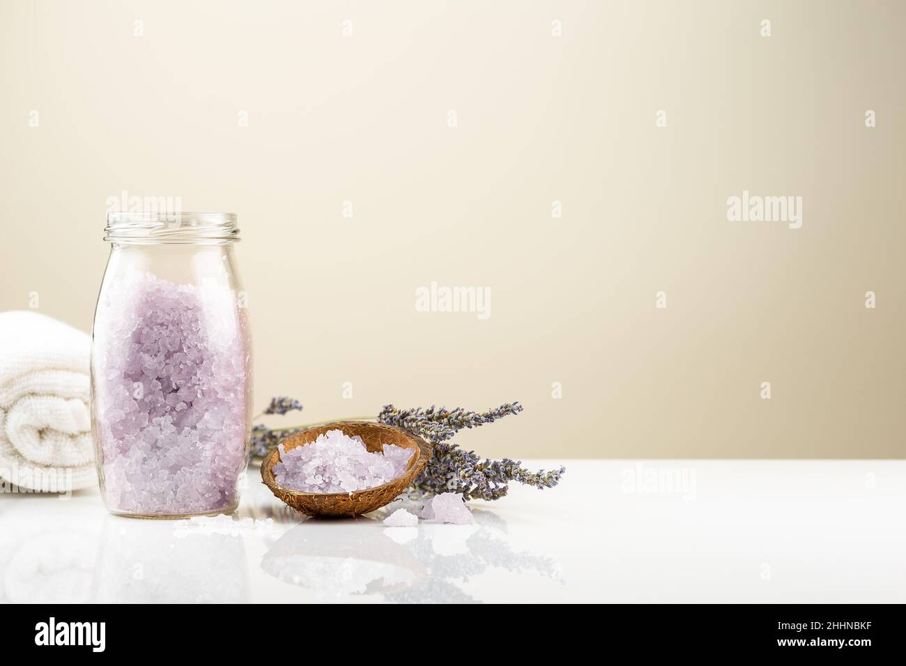 Lavendel-Badesalz in einem Glas mit einem Bund trockener Lavendelblüten und einem weißen Handtuch Stockfoto