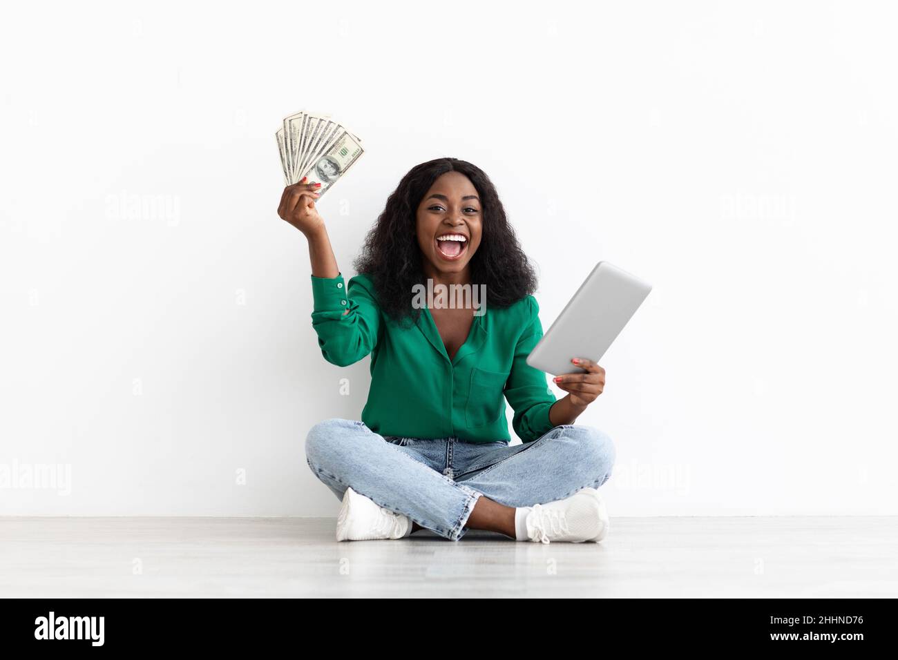 Reiche afroamerikanische Dame, die online spielt, Pad hält und Geld Stockfoto