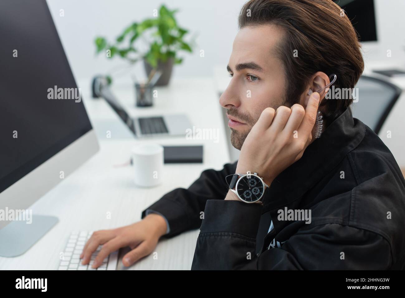 Ein ernsthafter Sicherheitsmann berührt den Kopfhörer, während er im Überwachungsraum arbeitet Stockfoto