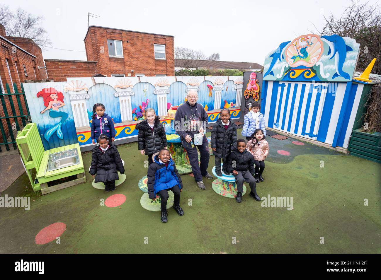 Birmingham, Großbritannien. 25th Januar 2022. Der Künstler Terry Glazebrook, 71, mit den Kindern der RC-Grundschule von St. Edmund, Spring Hill, Birmingham, als das von ihm geschaffene Spielplatzgemälde, um den langweiligen Blick auf die Innenstadt von Birmingham zu erhellen, steht vor der Fertigstellung. Laut einer Studie der Schools Week war die psychische Gesundheit die zweithäufigste unter den führenden Politikern (42 Prozent). Kinder aus innerstädtischen Gebieten gelten als am stärksten von psychischen Problemen bedroht. Kredit: Peter Lopeman/Alamy Live Nachrichten Stockfoto