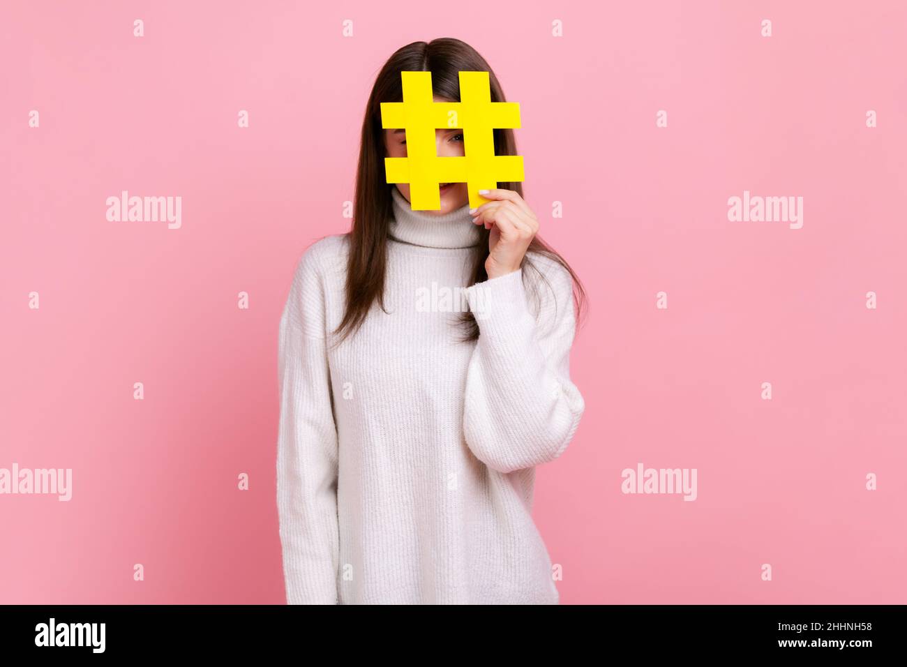 Weibliche Gesicht mit Social-Media-Hashtag-Symbol, empfehlen, trendige Inhalte folgen, Blog, tragen weißen lässigen Stil Pullover. Innenaufnahme des Studios isoliert auf rosa Hintergrund. Stockfoto