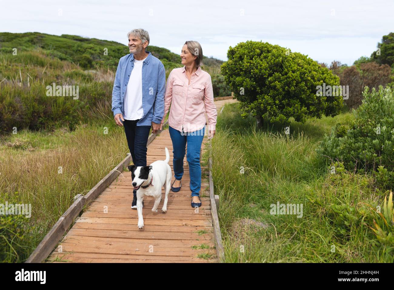 Glückliches kaukasisches reifes Paar schaut weg, während er mit Hund auf dem Boardwalk spazierengeht. Zweisamkeit, Wochenende und Naturkonzept. Stockfoto