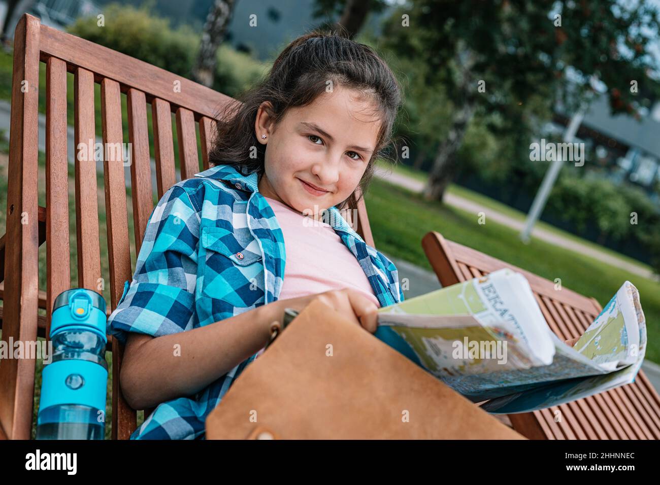 Positive junge Teenager-Mädchen mit einer Karte ruht auf einer Parkbank. Reisen im Sommerurlaub. Stockfoto