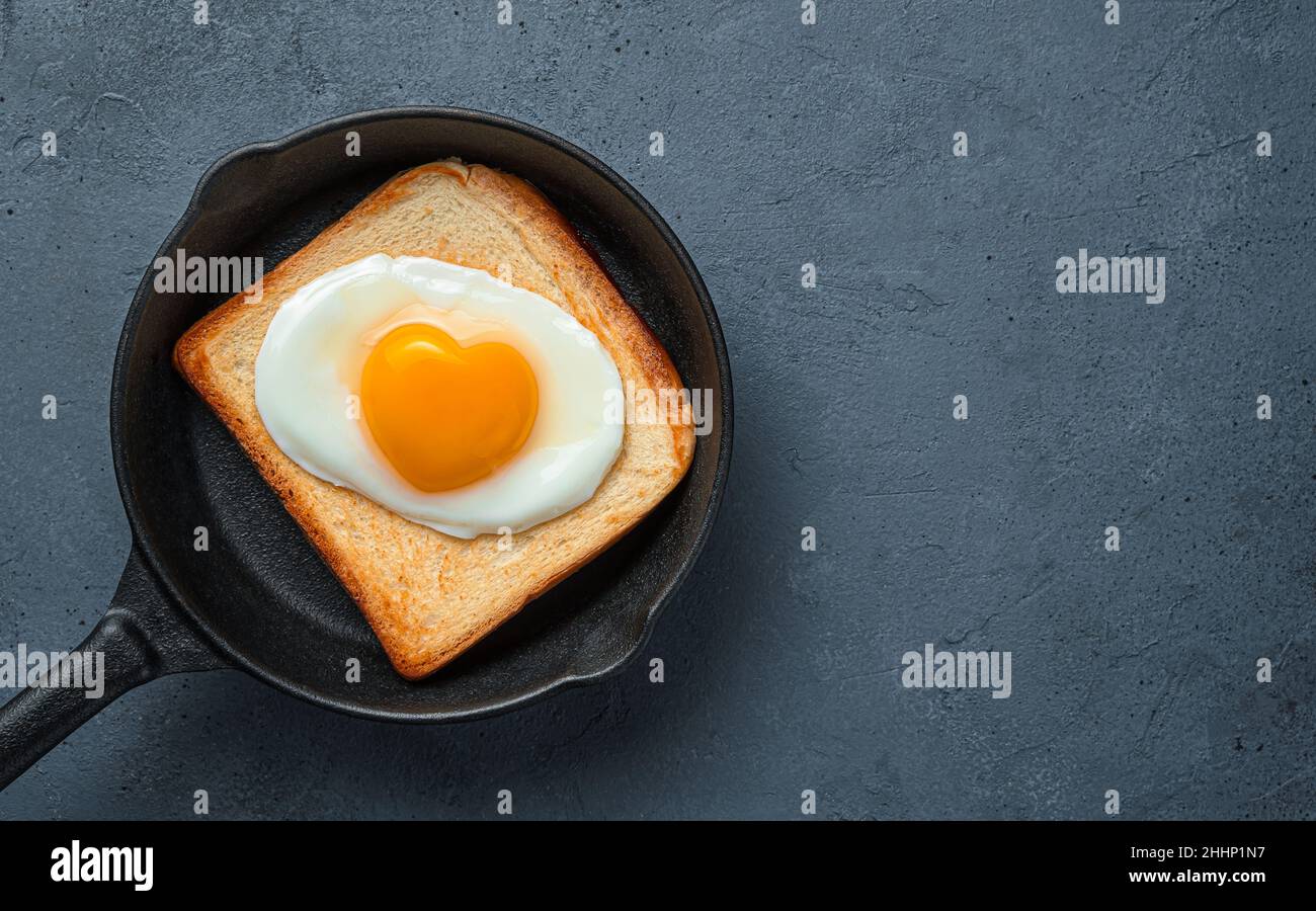 Spiegeleier mit herzförmigem Eigelb auf Toast in einer Pfanne. Stockfoto