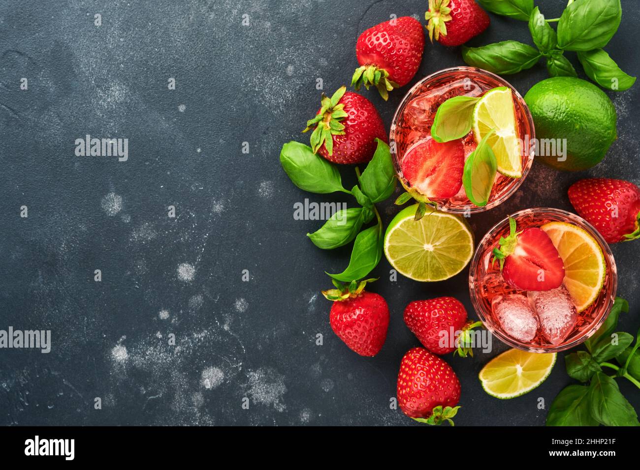 Zwei Gläser Punsch und frische Zutaten für die Herstellung von Limonade, infusem Detox-Wasser oder Cocktail. Erdbeeren, Limette, Minze, Basilikum, Eiswürfel und Shaker Stockfoto