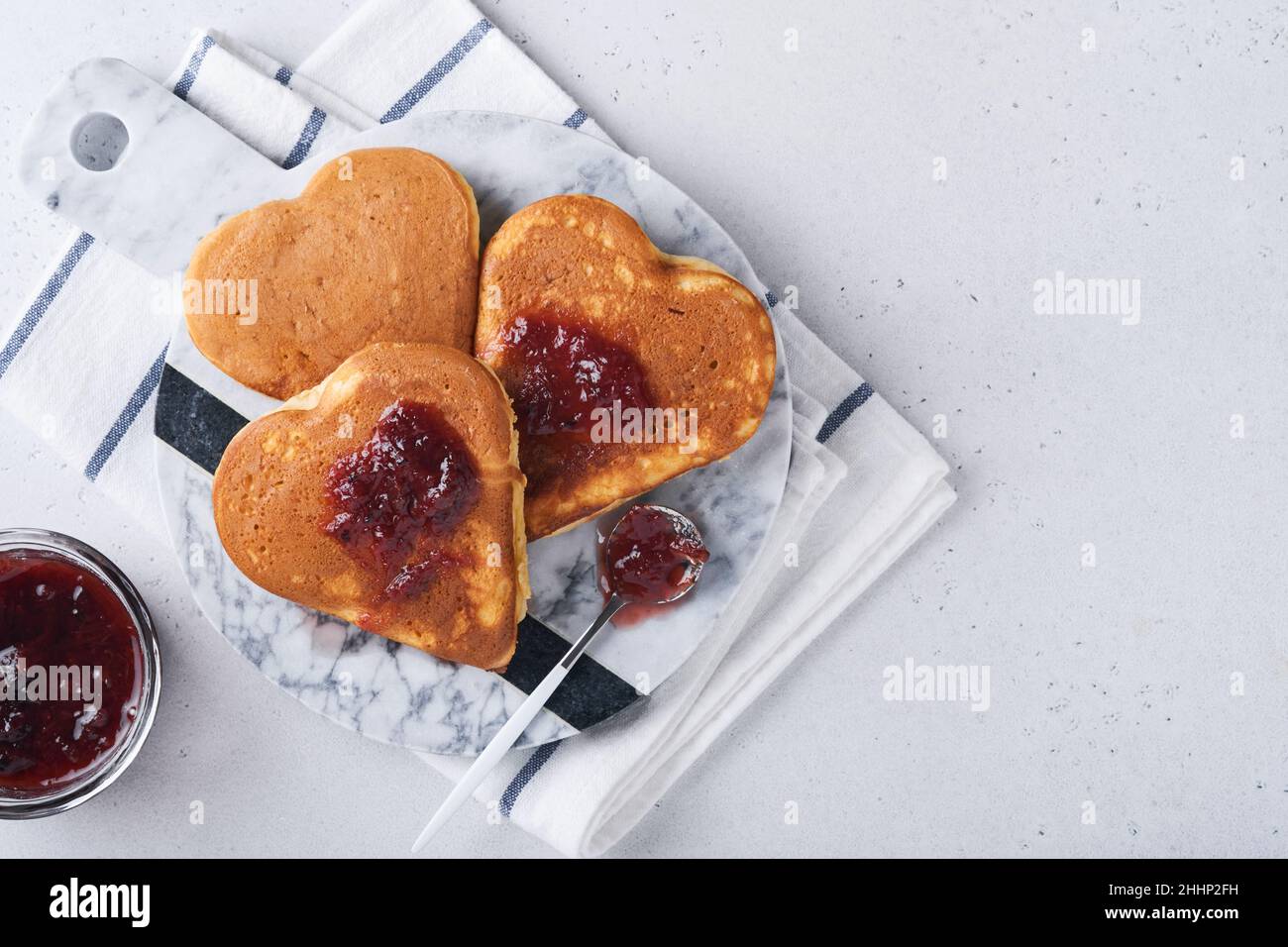 Zwei herzförmige Pfannkuchen mit Beerenmarmelade auf weißem Teller. Konzept eines festlichen Frühstücks zum Valentinstag oder einer angenehmen Überraschung für die Liebsten. Tisch vie Stockfoto