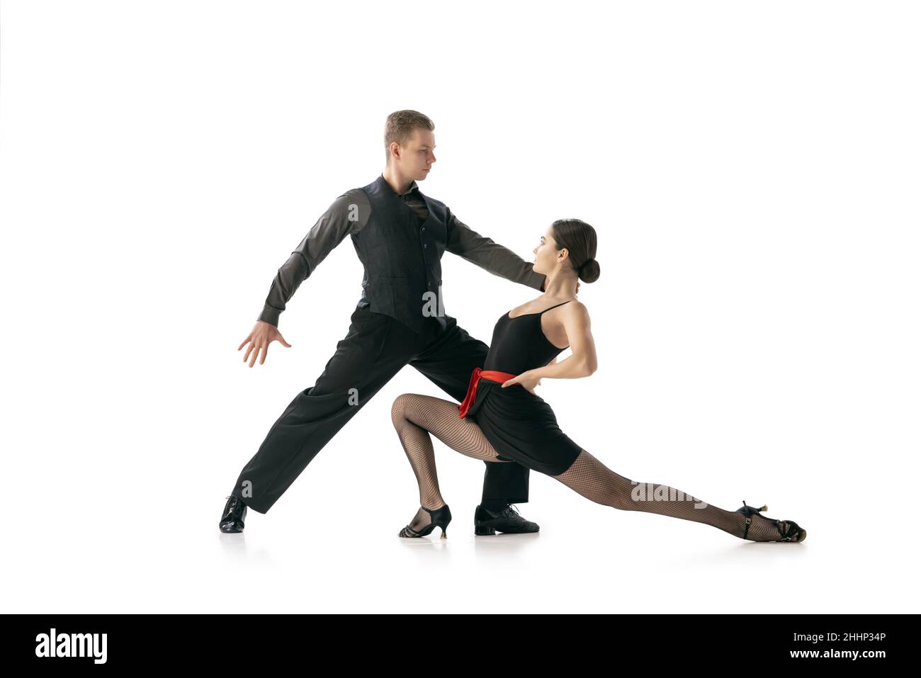 Dynamisches Porträt von flexiblen jungen Tänzern, die argentinischen Tango tanzen, isoliert auf weißem Studiohintergrund. Künstler in schwarzen Bühnenkostümen Stockfoto