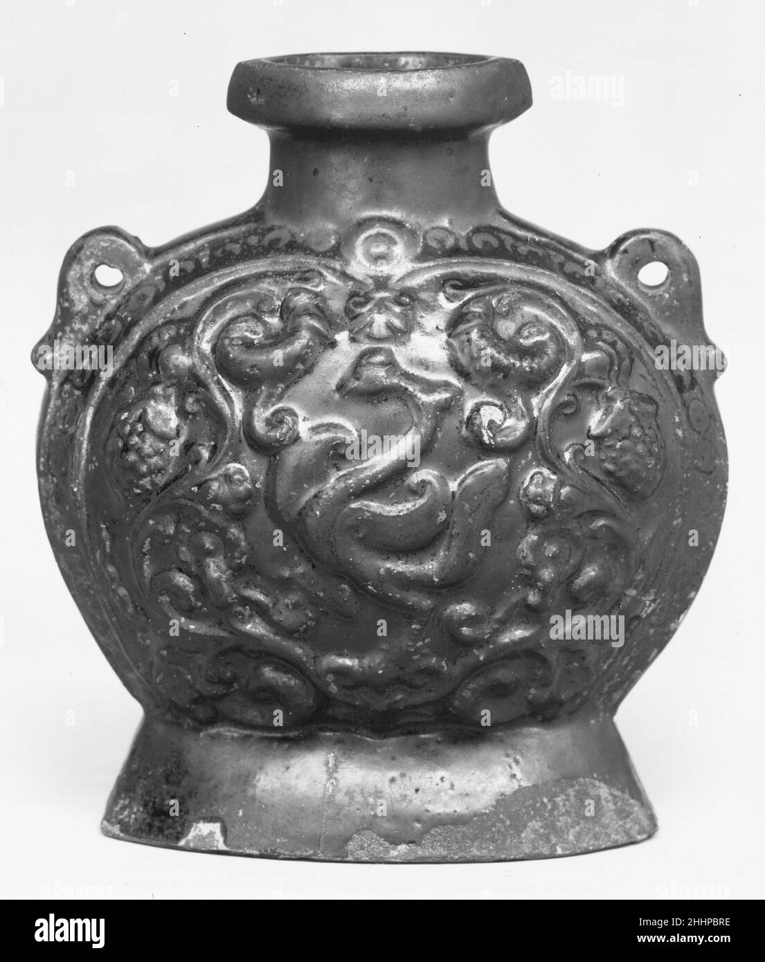 Flasche mit geformter Dekoration ca. Ende 6th–7th Jahrhundert China das von Schimmel geprägte Design auf beiden Seiten dieser beiden Gläser suggeriert das klassische griechische Ornament. Das dekorative Motiv der rollenden Weinrebe hat einen ultimativen hellenistischen Prototyp, der vom Westen über Zentralasien bis nach China zurückverfolgt werden kann. Dieses Design wurde in der Zeit der sechs Dynastien (220–589) in verschiedene Arten von Kunst in das chinesische dekorative Repertoire aufgenommen. (Der Tradition zufolge wurde die domestizierte Traube selbst im zweiten Jahrhundert v. Chr. aus dem Westen nach China eingeführt.) Kolben mit geformter Dekoration 52563 Stockfoto