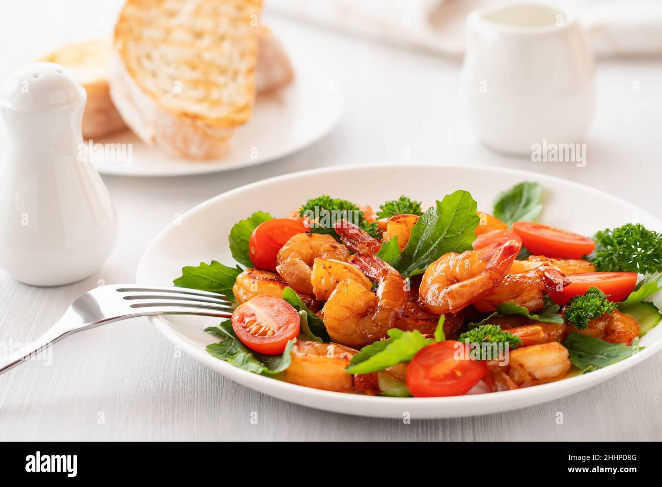 Frischer Salat aus Garnelen, Tomaten, Rucola und Kräutern auf einem weißen Teller Stockfoto