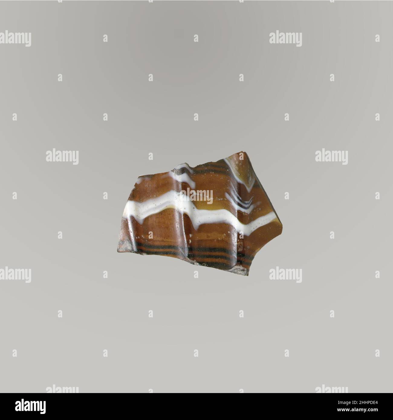 Glasmosaik geripptes Schalenfragment Ende des 1st. Jahrhunderts v. Chr.–Anfang des 1st. Jahrhunderts n. Chr. römisches Körperfragment. Lichtdurchlässiges honigbraun, kobaltblau und opakes weiß. Konvex geschwungene Seite, die sich nach unten verjüngt. Außen drei vertikale Rippen, recht weit auseinander, mit abgeflachten Oberteilen, Nach unten expandierend. Poliertes Äußeres; Lochfraß von Oberflächenblasen auf der Außenseite; cremig schillernde Verwitterung auf der Innenseite; schillernde Kanten. Glasmosaik gerippte Schale Fragment. Roman, l Stockfoto