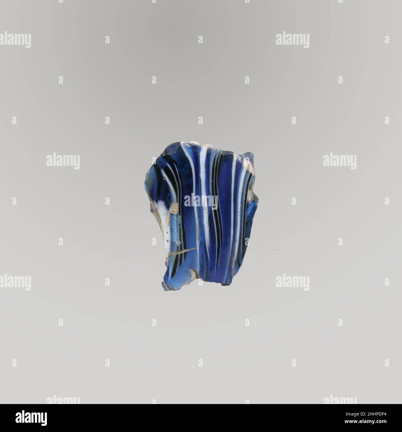 Glasmosaik geripptes Schalenfragment Ende des 1st. Jahrhunderts v. Chr.–Anfang des 1st. Jahrhunderts n. Chr. römisches Körperfragment.Durchscheinendes Blau und opakes Weiß.fast gerade Seite.Mosaikmuster aus Abschnitten eines einzigen Rohres in blauem Grund mit unregelmäßigen weißen und blauen Fäden in parallelen Linien gebildet; Außen zwei vertikale Rippen, mit abgeflachten Oberteilen und vielen horizontalen Werkzeugmarkierungen. Innen poliert; innen mit Lochfraß von Oberflächenblasen; innen stumpfend und cremig schillernde Verwitterung außen und gezackte Kanten. Glasmosaik gerippte Schale Fragment. Römisch. Spätes 1st Jahrhundert B.C.–frühes 1st Jahrhundert A.D.. Glas; Guss und Stockfoto