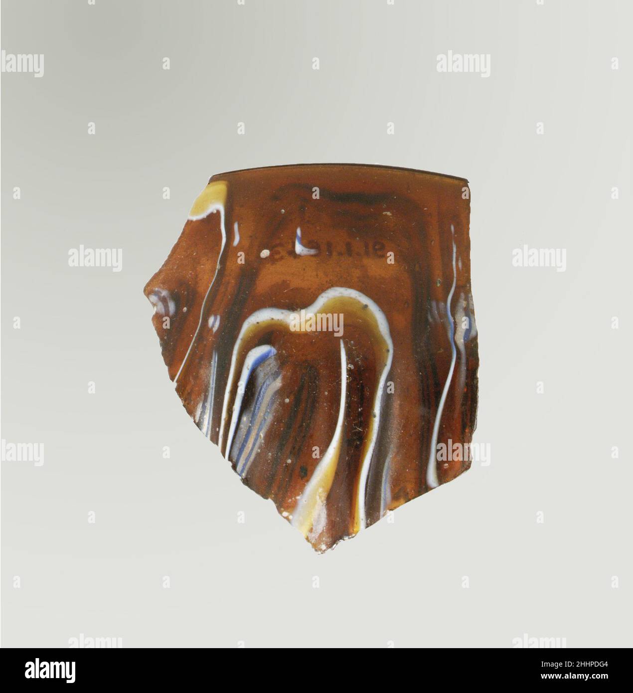Glasmosaik gerippte Schale Fragment Ende 1st Jahrhundert v. Chr.–Anfang 1st Jahrhundert n. Chr. Roman Rim Fragment.Translucent honigbraun, kobaltblau und opak weiß.Vertikaler, abgerundeter Rand; oben, Gerade Seite, dann auswölben mit konvexem gebogenen Profil.Spiralmosaik-Muster aus Abschnitten eines einzelnen Rohres in braunem Boden mit unregelmäßigen weißen und blauen Fäden in parallelen Linien gebildet; an der Außenseite zwei vertikale Rippen, mit abgeflachten Spitzen und abgerundeten Außenkanten, nach unten zulaufend.Polierte Außenseite; Lochfraß von oberflächlichen Blasen auf der Außenseite; stumpfende und cremig schillernde Verwitterung auf der Innenseite, am Rand und ja Stockfoto