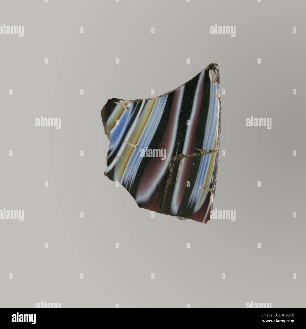 Glasmosaik geripptes Schalenfragment Ende des 1st. Jahrhunderts v. Chr.–Anfang des 1st. Jahrhunderts n. Chr. römisches Körperfragment.Durchscheinendes Lila, Blau, opakes Weiß und Gelb.Teil der Seite, oben nach außen abfackeln und nach unten zuwinken.Mosaikmuster aus Abschnitten eines einzelnen Rohres in purpurem Boden mit weißem, gelbem, Und blaue Fäden in parallelen vertikalen Linien; an der Außenseite Teile von zwei abgerundeten Rippen, mit unregelmäßigen Werkzeugspuren über die Oberseite.gebrochen in der rechten unteren Ecke und repariert; polierte Innenseite; leichte Lochfraß und Verwitterung von Oberflächenblasen; stumpfende und schillernde Verwitterung an der Außenseite und Zacke Stockfoto