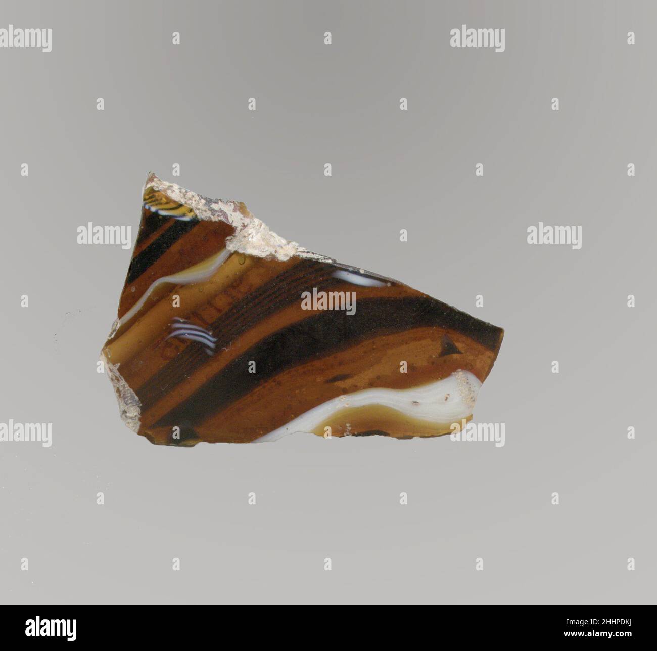 Glasmosaik-Schalenfragment Ende des 1st. Jahrhunderts v. Chr.–Anfang des 1st. Jahrhunderts n. Chr. römisches Körperfragment.Durchscheinendes honigbraun, kobaltblau und opakes Weiß.konvex geschwungene Seite.Mosaikmuster aus Abschnitten eines einzelnen Rohres in braunem Boden mit unregelmäßigen welligen weißen und blauen Fäden in parallelen Linien. Lochfraß von Oberflächenblasen auf der Außenseite; stumpfende und cremig schillernde Verwitterung auf der Außenseite und gezackte und abgebropfte Kanten. Fragment der Glasmosaik-Schale. Römisch. Spätes 1st Jahrhundert B.C.–frühes 1st Jahrhundert A.D.. Glas; Guss. Frühkaiserlich. Glas Stockfoto