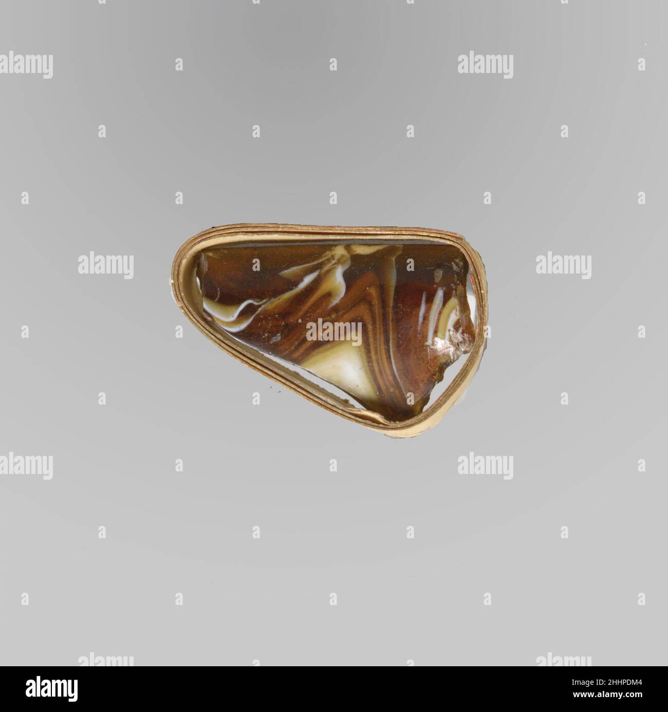 Fragment der Glasmosaik-Schale Ende 1st. Jh. v. Chr.–Anfang 1st. Jh. n. Chr. Fragment des römischen Rands.Durchscheinendes honigbraun und opakes Weiß.dicker, ausgespielter Rand mit leicht abgeschrägter Lippe; seitlich nach unten verjüngend.Mosaikmuster aus einer oder mehreren Stöcken in braunem Boden mit welligen weißen Fäden in parallelen Linien. Polierter Innenraum; Lochfraß von Oberflächenblasen auf dem Innenraum; stumpfende und cremig schillernde Verwitterung auf der Außenseite, Unterseite des Randes und gezackte Kanten. Fragment der Glasmosaik-Schale. Römisch. Spätes 1st Jahrhundert B.C.–frühes 1st Jahrhundert A.D.. Glas; Guss. Frühkaiserlich. Glas Stockfoto