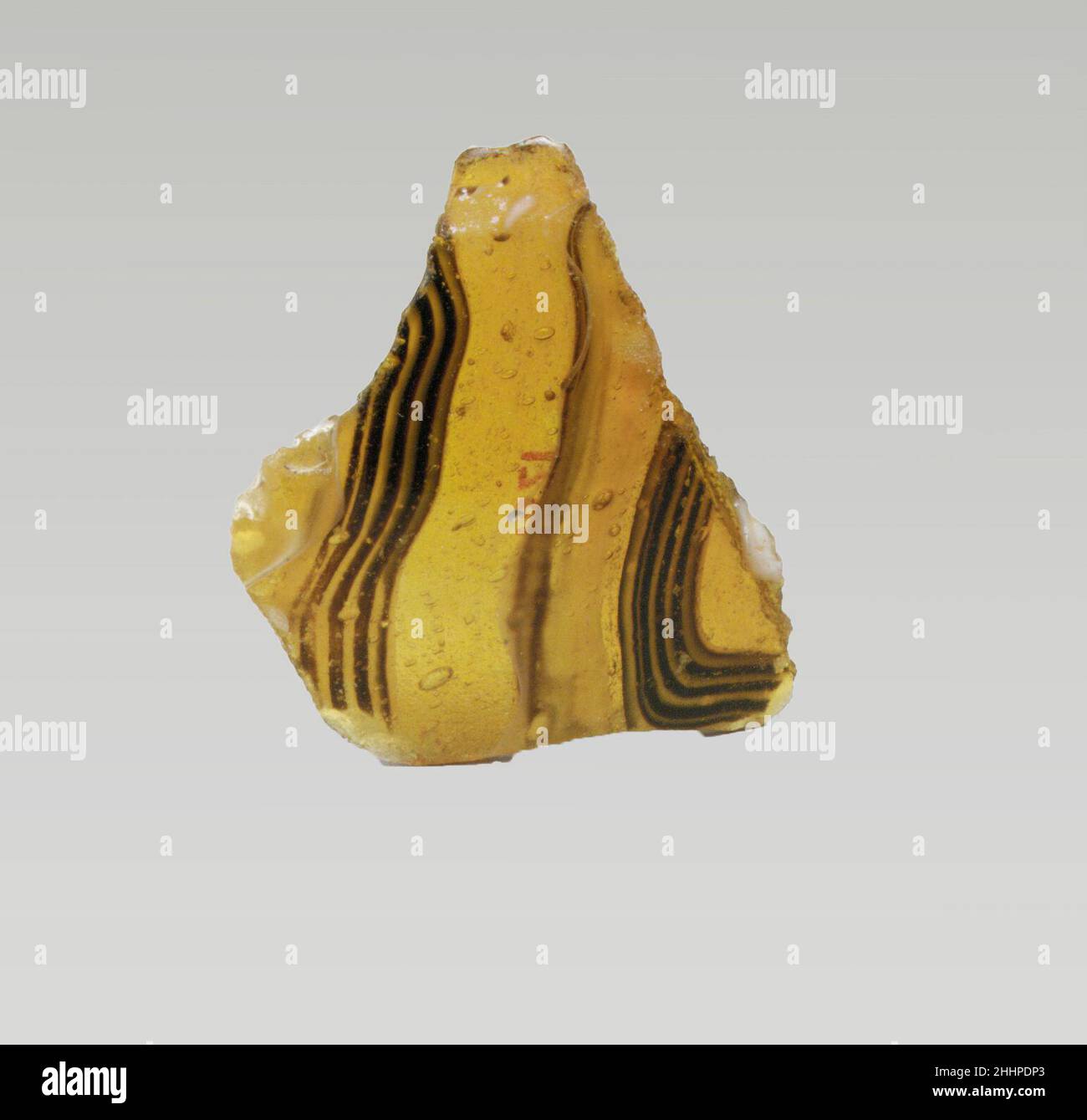 Glasmosaik-Schalenfragment Ende des 1st. Jahrhunderts v. Chr.–Anfang des 1st. Jahrhunderts n. Chr. Römisches dünnwandiges Körperfragment.Durchscheinendes honigbraunes, blaues, violettes und opakes Weiß.konvex geschwungene Seite.Mosaikmuster aus Bändern, die aus Längen von zwei oder mehr Stöcken in einem braunen Boden mit welligen weißen, blauen und violetten Fäden in parallelen Linien gebildet werden. Poliertes Äußeres; Lochfraß von Oberflächenblasen an der Außenseite; stumpfende und cremig schillernde Verwitterung an der Innenseite und gezackte Kanten. Fragment der Glasmosaik-Schale. Römisch. Spätes 1st Jahrhundert B.C.–frühes 1st Jahrhundert A.D.. Glas; Guss. Frühkaiserlich. Glas Stockfoto
