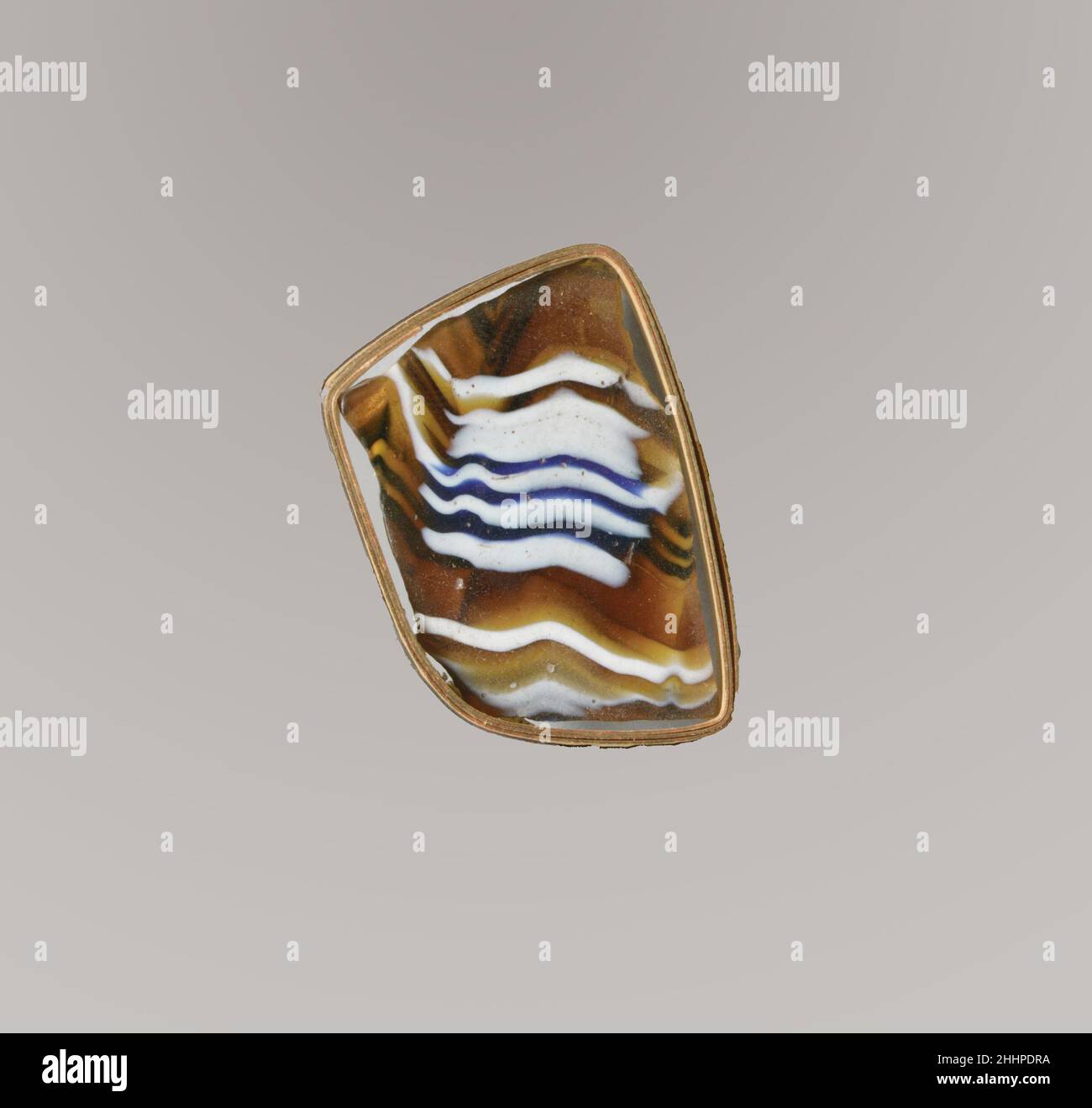 Glasmosaik geripptes Schalenfragment Ende des 1st. Jahrhunderts v. Chr.–Anfang des 1st. Jahrhunderts n. Chr. Römisches dünnwandiges Körperfragment. Lichtdurchlässiges Honigbraun, Kobaltblau und opakes Weiß. Wird oben in Richtung Rand ausgespielt; Gerade Seite nach unten zulaufend.Spiralmosaik aus Abschnitten eines einzelnen Rohres in braunem Boden mit weißen und blauen Fäden in parallelen horizontalen Linien gebildet; auf der Außenseite Teile von drei flachen vertikalen Rippen, nach unten zulaufend, mit Werkzeugmarkierungen über der Oberseite der zentralen Rippe.Polierte Innenseite; Lochfraß von Oberflächenblasen; Dullend, cremig verwittert und leicht schillernd auf der Außenseite und gezackt Stockfoto