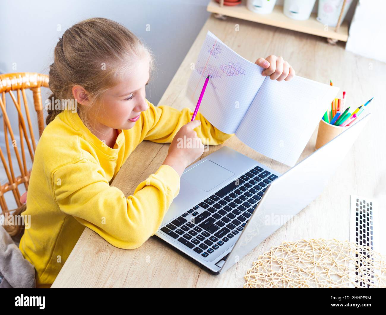 Kaukasische süße Schülerin im gelben Sweatshirt, die ihre Mathe-Hausaufgaben zu Hause vor dem Laptop macht und dem Lehrer das gelöste Beispiel auf dem Bildschirm zeigt. E Stockfoto