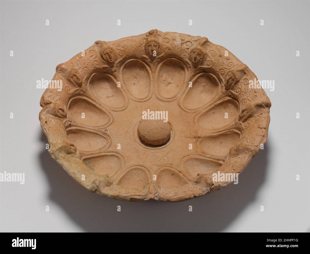 Terracotta phiale (Libation Bowl) 3rd. Jahrhundert v. Chr. Griechisch, Süditalien, Apulien Diese charakteristische Art von phiale mit zwölf eiförmigen Hohlräumen und Reliefschmuck auf dem Rand stammt von Metallprototypen, die in der archaischen Zeit aus dem Osten nach Griechenland eingeführt wurden. Die hellenistische Form wird in sehr seltenen Silberbeispielen bestätigt. Die zahlreichen Terrakotta-Pendants, die überleben, sind vor allem mit Tarentum verbunden. Köpfe von Orientalen wechseln sich mit Scrollwork um den äußeren Rand ab. Terracotta phiale (Libation Bowl) 250805 Griechisch, Süditalien, Apulien, Terracotta phiale (Libation Bowl Stockfoto