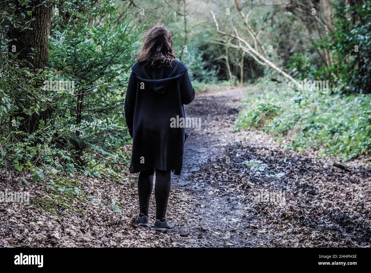 Moody geheimnisvolles Bild einer Frau, die durch einen schlammigen Pfad in einem leeren Wald geht, aufgenommen im Scadbury Park Nature Reserve, 11.. Februar 2018 Stockfoto