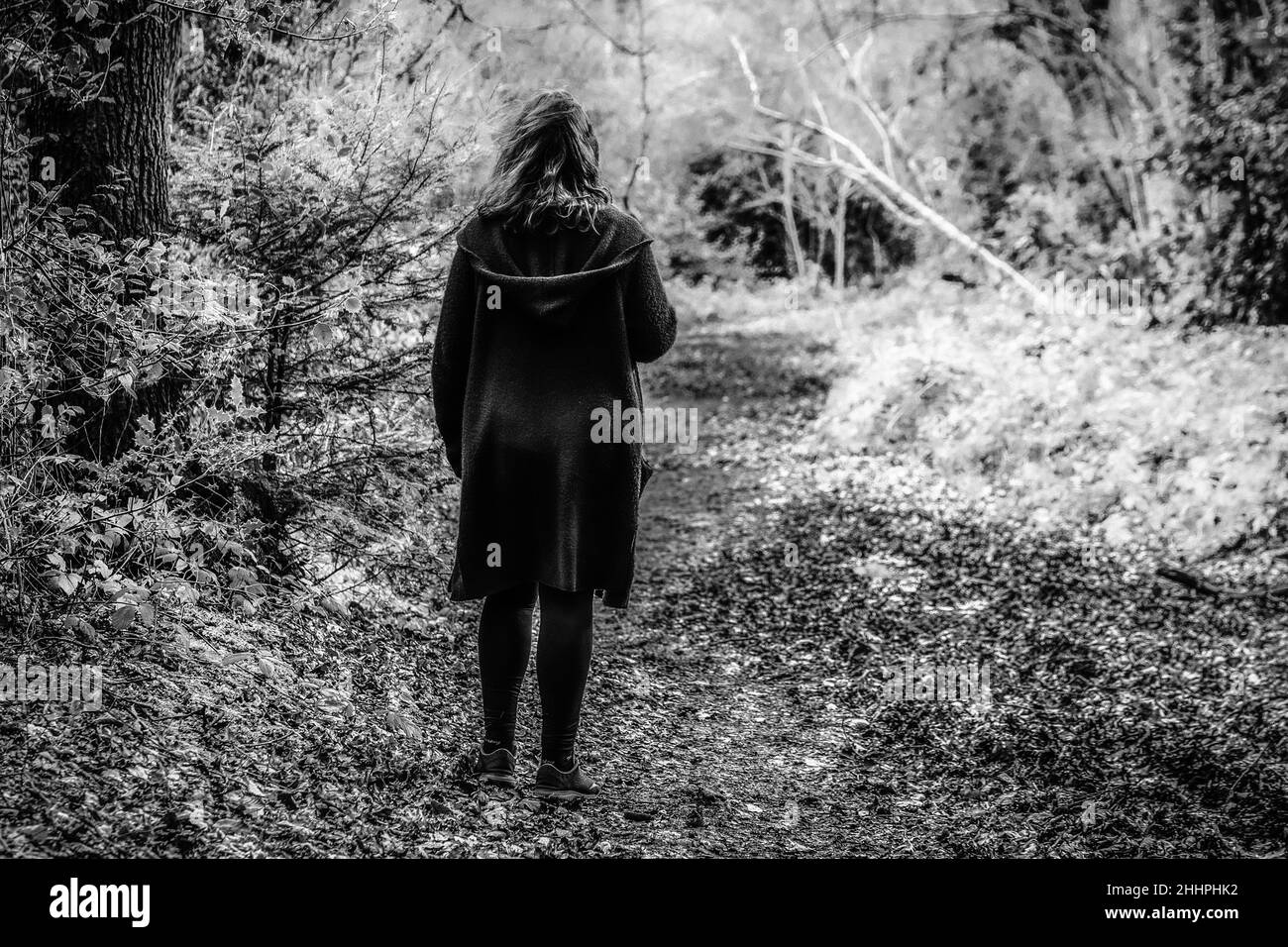 Moody geheimnisvolles Bild einer Frau, die in einem S/W-Ton durch einen schlammigen Pfad in einem leeren Wald geht, aufgenommen im Scadbury Park, 11.. Februar 2018 Stockfoto