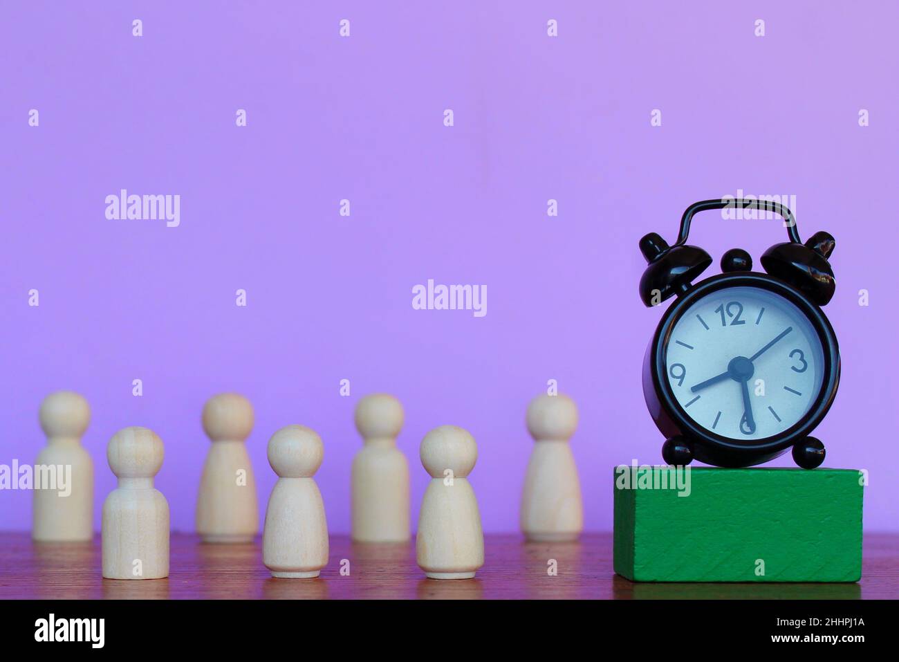 Arbeitszeit, Stundenlohn, Terminkonzept. Wecker und Holzpuppen auf violettem Hintergrund. Stockfoto