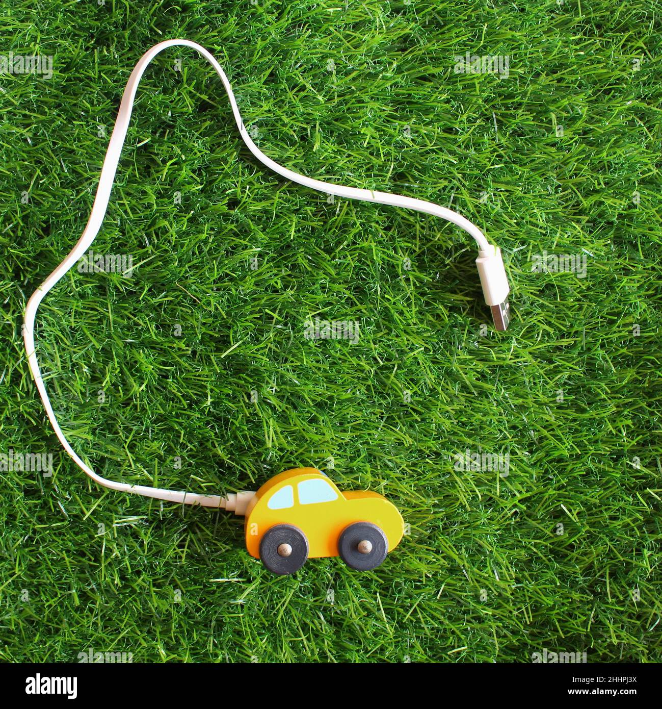 EV oder Elektroauto kreatives Konzept. Spielzeugauto und Strombankkabel auf grünem Gras. Stockfoto