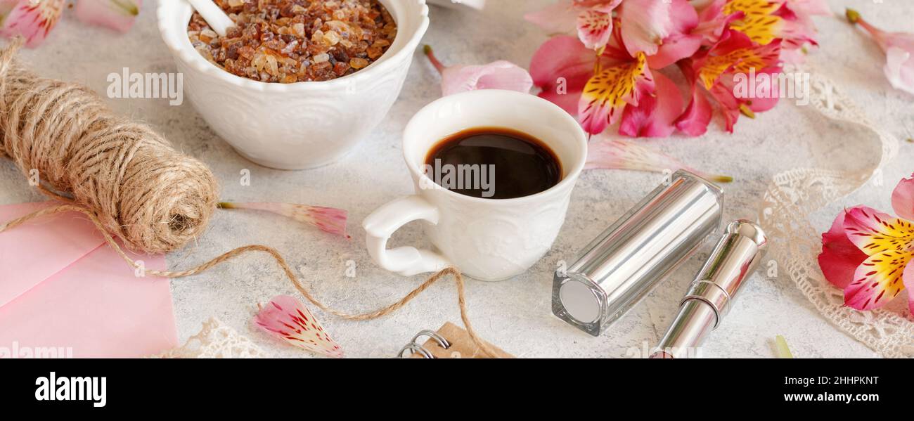 Kaffeetasse in der Nähe von rosa Blumen, Lippenstift und Umschlag auf weißem Tisch Nahaufnahme. Romantisches Frühstück Stockfoto