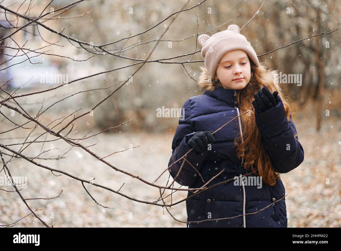 Nettes kleines Mädchen hält einen Baum Ast ohne Blätter auf einem Hintergrund von fallenden Schneeflocken. Erstes Schneekonzept. Stockfoto