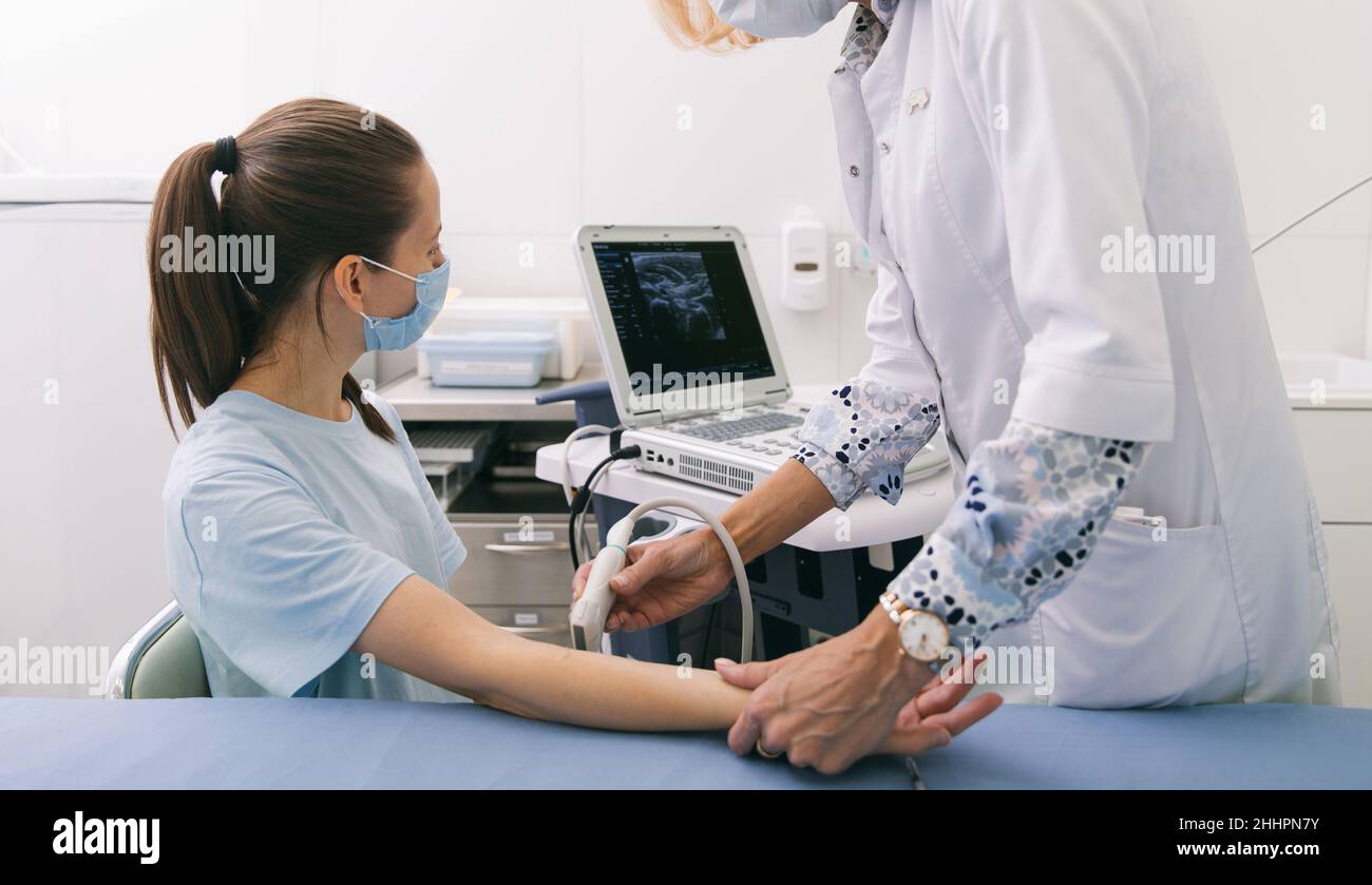 Arzt, der den Ultraschall an der Hand macht, Nahaufnahme. Der Arzt zeigt dem Patienten Ultraschallergebnisse. Medizinische Ultraschalluntersuchung. Rehabilitation Stockfoto