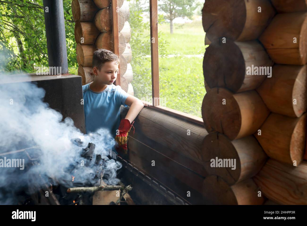 Das Kind zündet Feuerholz auf dem Grill im Pavillon in Karelia an Stockfoto