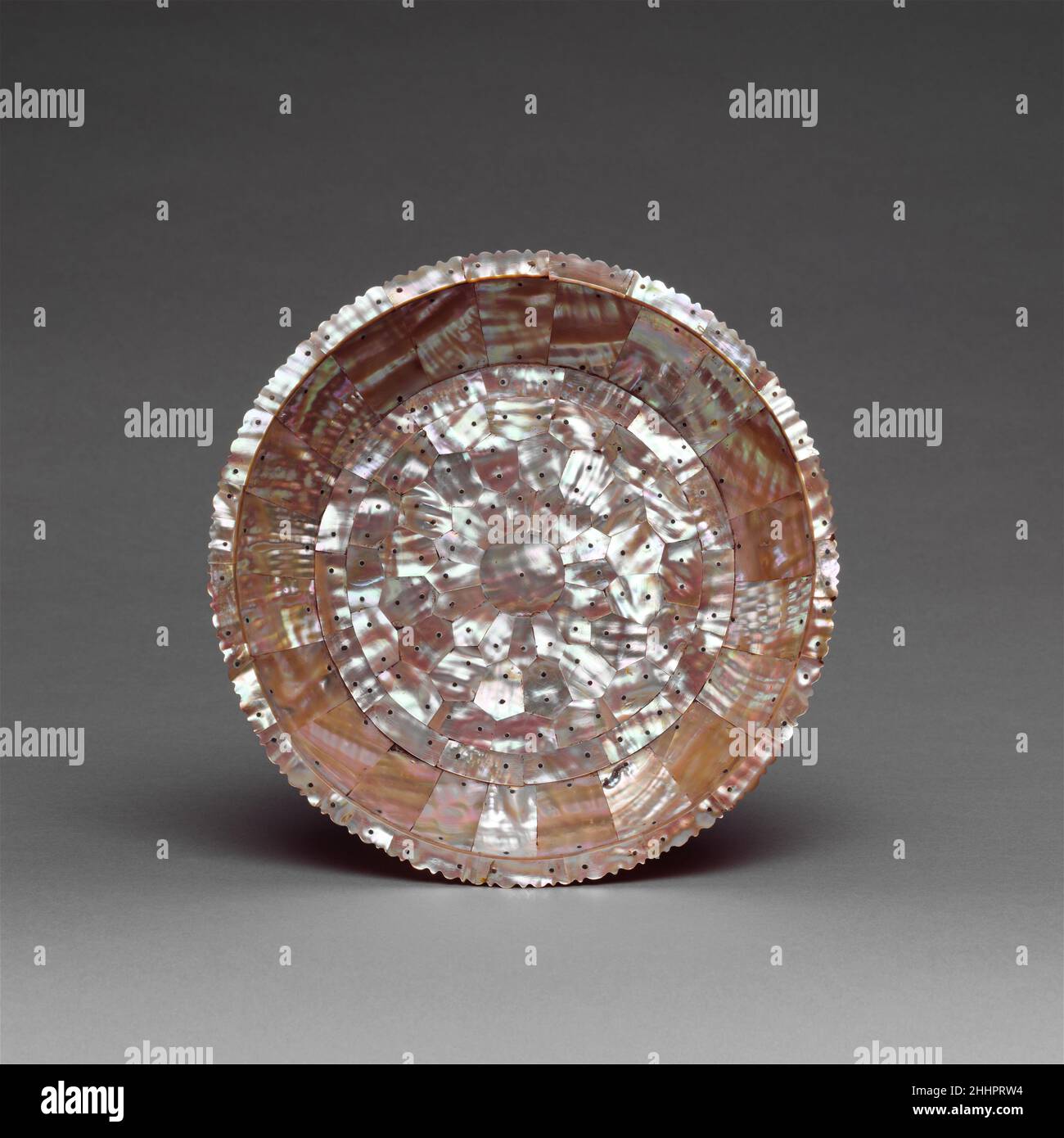 Platte Mitte des 16th.–17th. Jahrhunderts Indien (Gujarat) auf dieser Platte, die ein Holzsubstrat hat, wurde Perlenschale in verschiedenen Größen auf die Front und die Seiten aufgetragen und mit Stiften gesichert. Das Blumenmotiv in der Mitte findet sich oft auf solchen Gegenständen. In Gujarat wurden sowohl Platten als auch Außenbleche und Becken, viele in Formen, die von europäischen Schiffen abgeleitet wurden, für den portugiesischen Handel hergestellt. Das einzige datierte Beispiel ist eine Platte in Lissabon, auf der das Jahr 1568 in den Boden eingeschnitten ist. Beispiele sind auch aus königlichen Sammlungen in Dresden, Paris und London bekannt. Platte 73309 Stockfoto