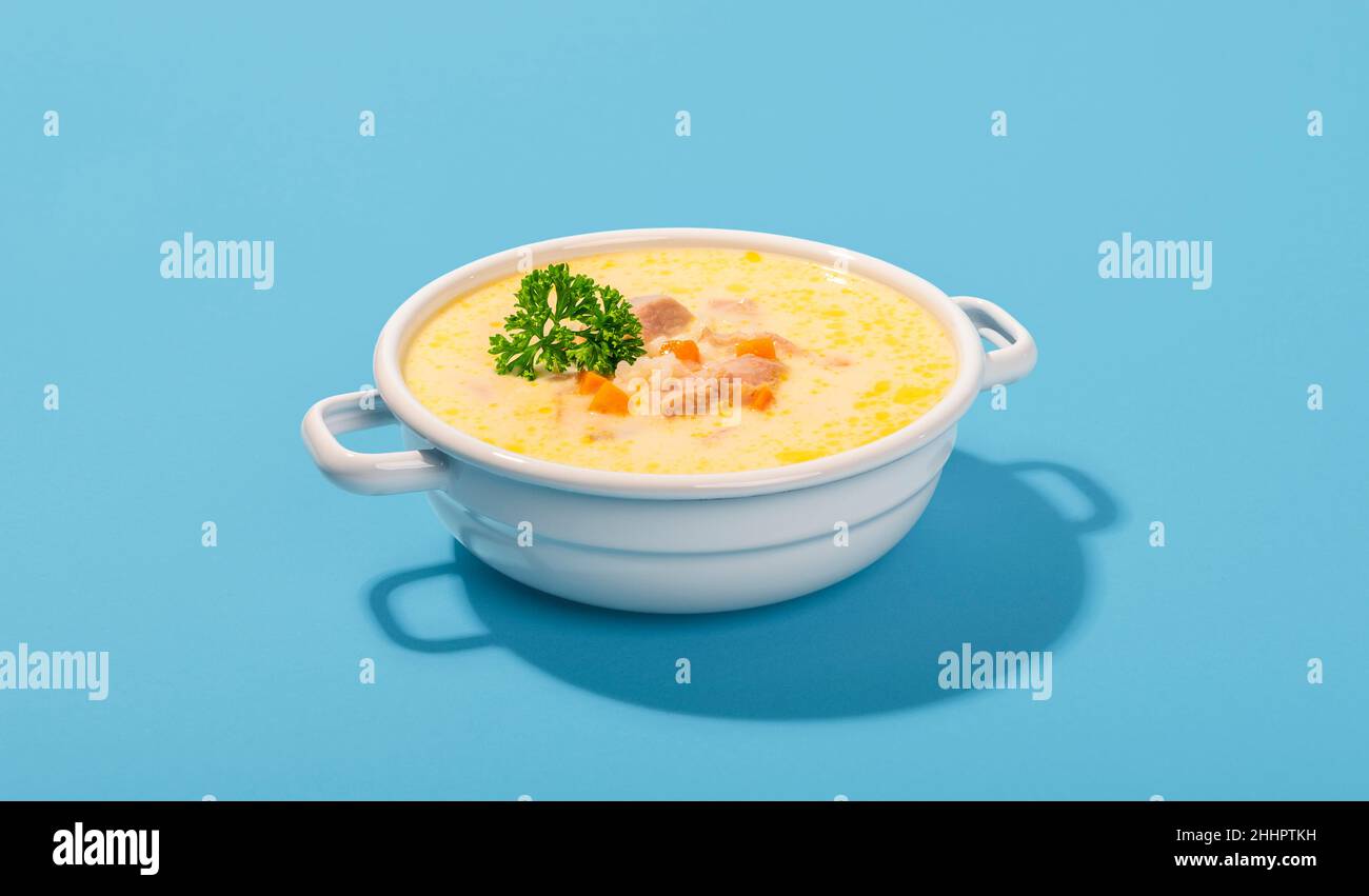 Schüssel mit köstlicher griechischer Suppe mit Karotten, Hühnerfleisch und Zitronensaft. Emaille-Schüssel mit Hühnersuppe isoliert auf blauem Hintergrund. Stockfoto