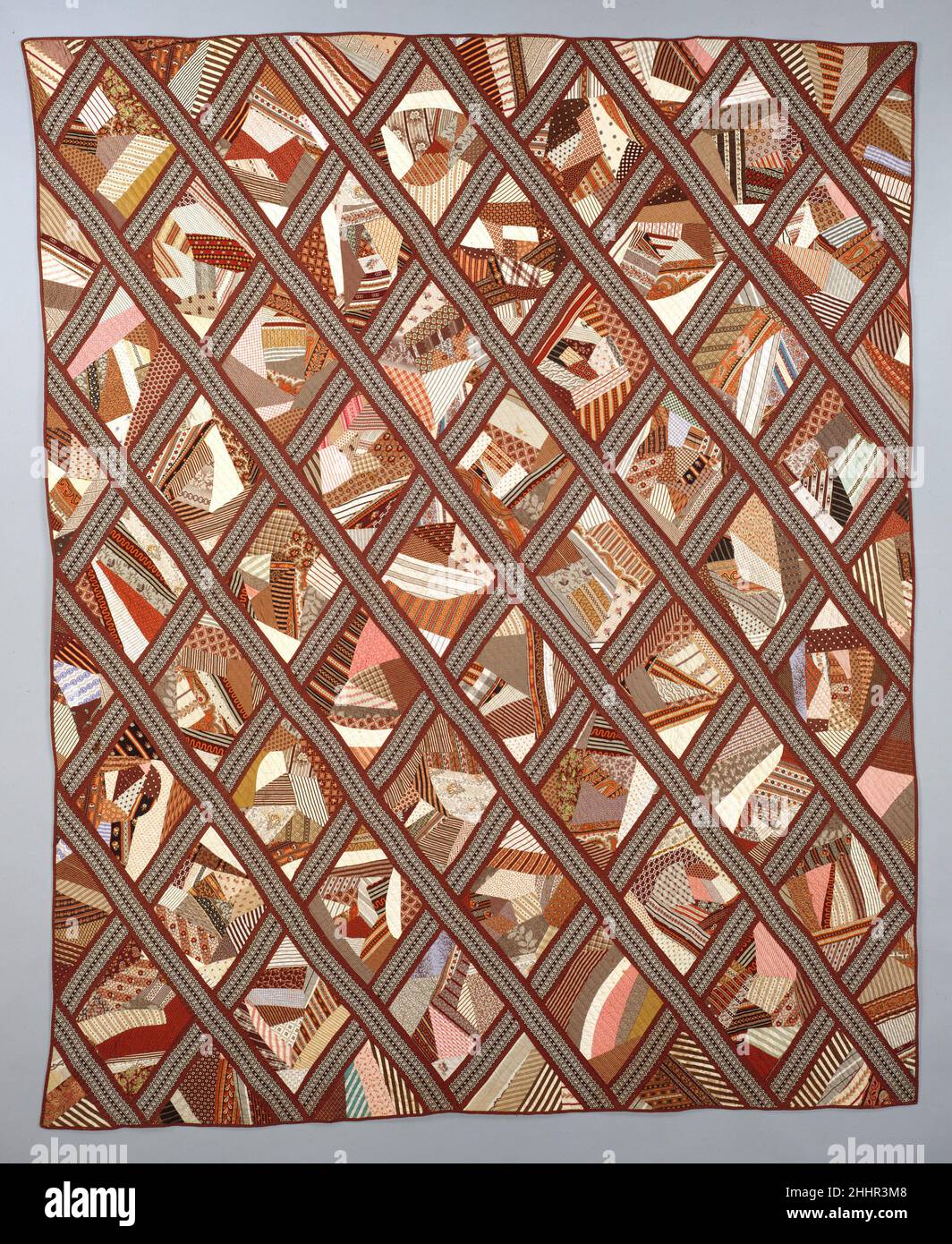 Quilt, enthaltenes Crazy Pattern 1872 Nancy Doughty die diamantförmigen Crazy Blocks dieser Quilt sind aus einer Vielzahl von braun, orange und rosa bedruckten Baumwolle zusammengesetzt. Die Blöcke sind mit braun und schwarz bedruckten Baumwolleinlagen verbunden. Die Blöcke werden mit der Nähmaschine an die Verzurrung geheftet; der Rest der Steppdecke wird von Hand genäht. Das Trägergewebe ist aus einer weißen Baumwolle, die mit einem kleinen braunen Gitter bedruckt ist. Das Stück ist über seine gesamte Oberfläche mit diagonalen parallelen Linien gesteppt. Quilt, enthielt Crazy Muster. Amerikanisch. 1872. Baumwolle. Wahrscheinlich hergestellt in Maryland, USA Stockfoto
