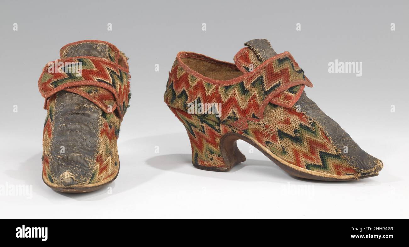 Schuhe 1700–1729 Britisches kühnes geometrisches Wollleinwand-Werk, bekannt als bargello oder Flammenstich, war Ende des 17th. Und 18th. Jahrhunderts ein wichtiger Stickereistil. Hauptsächlich für Polsterungen und kleine persönliche Accessoires wie Geldbörsen (zum Beispiel 2009.300.1782) verwendet, wird es hier in einem typischen Zickzack-Muster auf diesem Paar von Damen-Latchet-Schuhen gesehen. Es ist bemerkenswert, dass auch die Ferse mit der Nadelarbeit bedeckt ist, da es eher typisch ist, eine kontrastierende Seide oder Leder verwendet zu finden. Der breite Streifen aus Metallgeflecht, der in der Mitte des Vamps entlang lief, war zu dieser Zeit ein vorherrschendes Dekorationsmotiv. Als Stockfoto