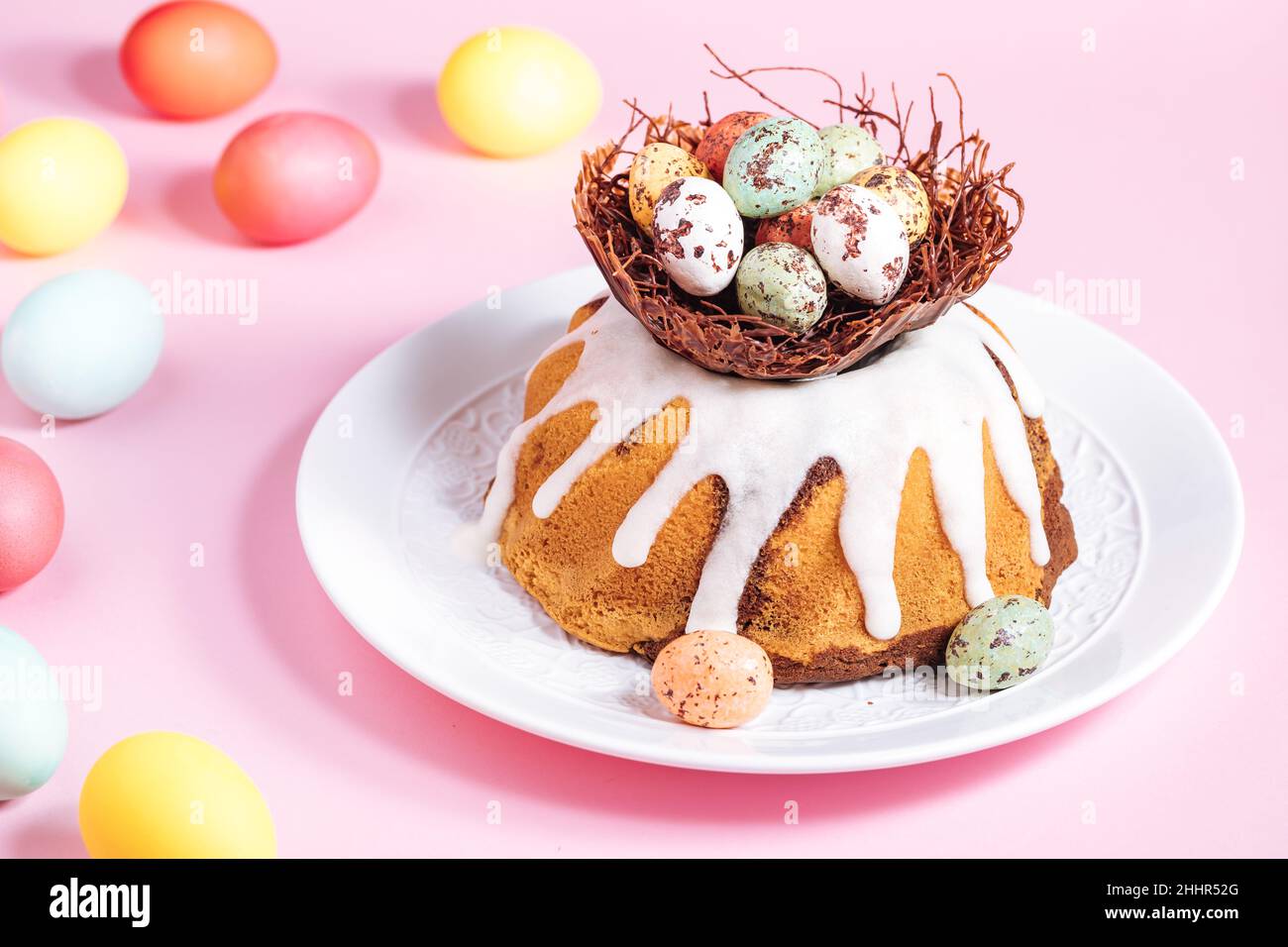 Osterkuchen mit bunten Eiern in einem Schokoladennest auf rosa Hintergrund. Happy Easter Konzept. Dessert auch als Kuglof bekannt. Stockfoto