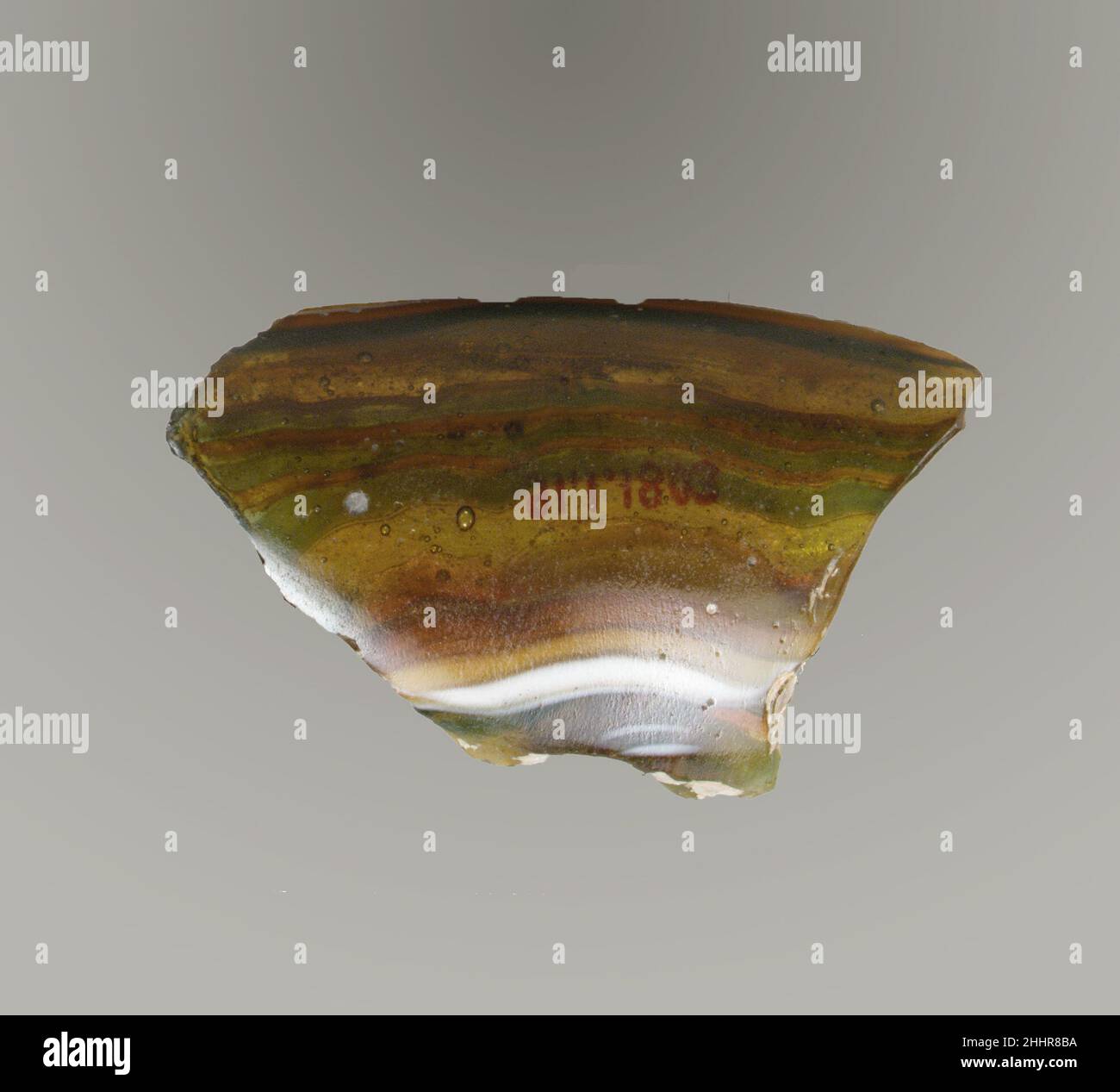 Fragment der gerippten Glasmosaik-Schale Ende des 1st. Jahrhunderts v. Chr.–Anfang des 1st. Jahrhunderts n. Chr. Fragment des römischen Rands. Lichtdurchlässiges honigbraun, teilweise mit Weiß gemischt und undurchsichtig gelb, kobaltblau und undurchsichtig weiß.ausgespielter Rand mit abgerundeter Lippe; Leicht gewölbte, nach unten gewölbte Seite.Mosaikmuster aus einer oder mehreren Stöcken in braunem Boden mit welligen blauen und weißen Fäden in parallelen Linien; außen Teil einer breiten vertikalen Rippe, mit abgeflachte und bearbeitete Oberseite.viele Blasen; polierte Innenseite; Lochfraß von Oberflächenblasen; Dullende und cremig schillernde Verwitterung Stockfoto
