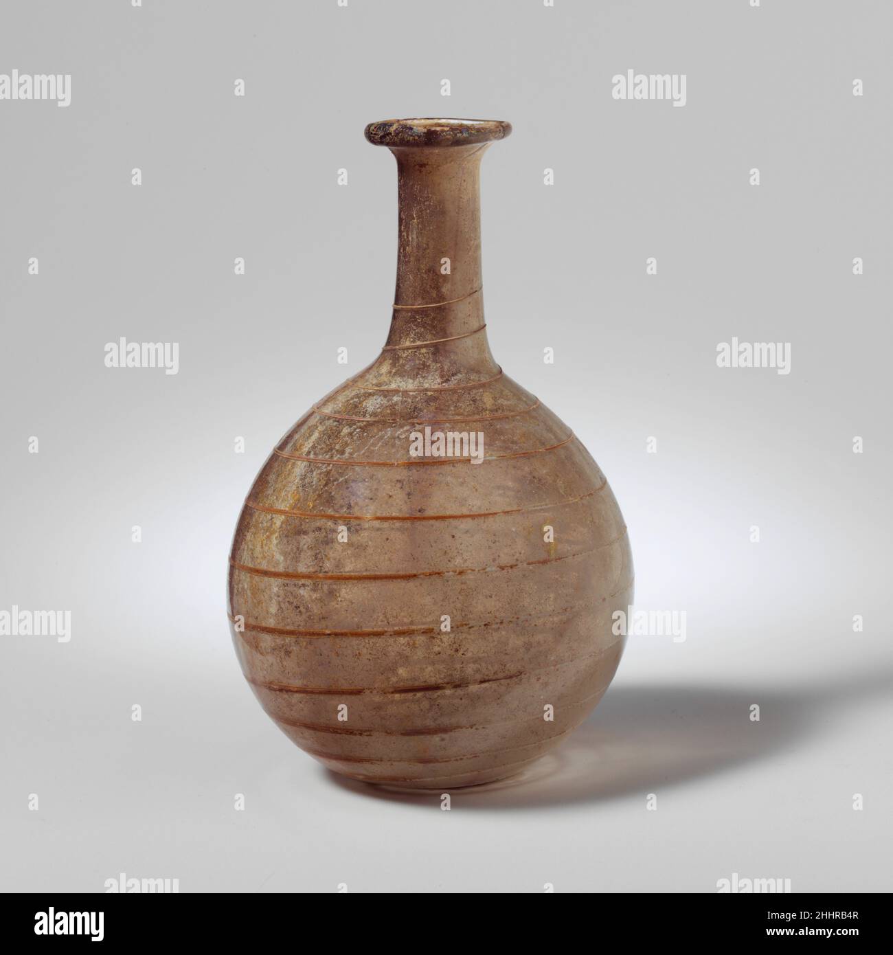 Parfümflasche aus Glas 1st. Jahrhundert n. Chr. römisch farblos mit violettem Farbton; Spur in opakes Weiß.Rand ausgeklappt, rund und innen; kurzer, auffaellender Mund; Zylindrischer Hals, leicht nach unten ausdehnend; kugelförmiger Körper; kleiner, abgeflachte Boden.einzelne Spur, die auf den Hals aufgetragen und in einer Spirale nach unten gezogen wird, dicker wird und am bottom.Complete endet, aber kleiner Bruch im Rand repariert; Nadelstich-Blasen; Lochfraß und schillernde Verwitterung. Parfümflasche aus Glas 239792 Stockfoto