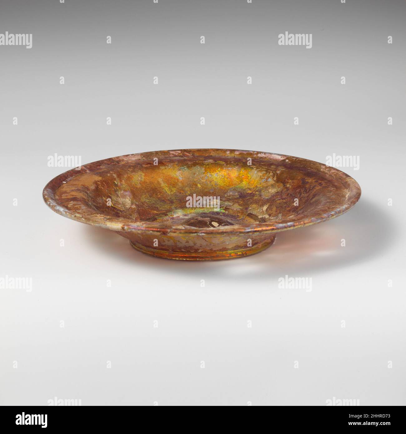 Glasschale 4th–5th century A.D. römisch farblos.Everted, Abfackeln, röhrenförmiger Rand, rund und nach unten gefaltet, mit breiter fast horizontaler Innenschulter; unregelmäßige S-förmige Seite zum Körper, in unebenem integralen röhrenförmigen Basisring gebogen; großer tritt im Boden.gebrochen und repariert, mit drei Löchern in der Seite; einige Nadelstich und größere Blasen; Tiefes Lochfraß und brillant schillernde Verwitterung.Mis-förmigen Basisring, so nicht sicher stehen.. Glasschale 239882 Stockfoto