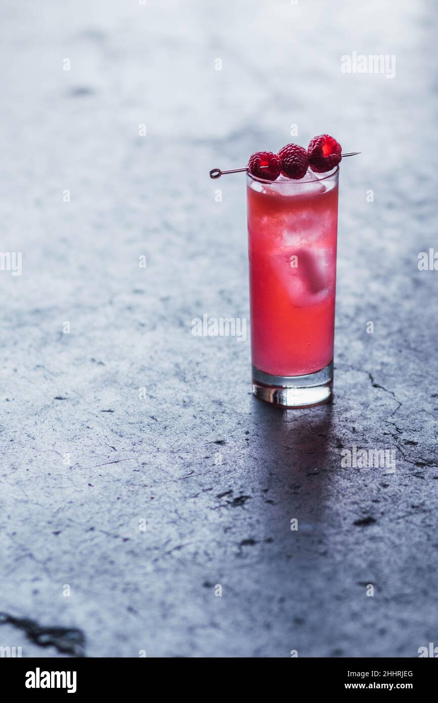 Hoher rosafarbener Cocktail-Drink mit drei Himbeeren auf Cocktail-Pick, auf Beton Stockfoto