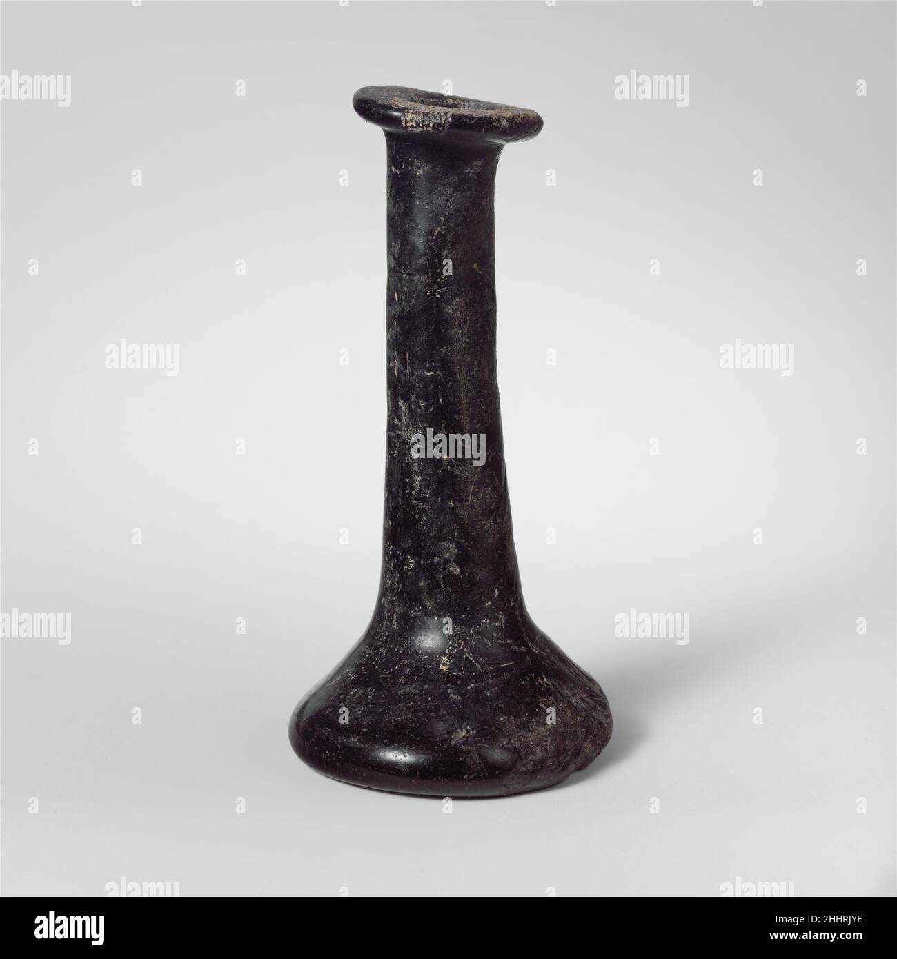 Parfümflasche aus Glas 2nd–4th Jahrhundert n. Chr. Römische Farbe unsicher, appering schwarz.breiter, schräge Rand, ausgeklappt, über, Und innen, oben abgeflacht, unregelmäßiger ovaler Mund bildet; uneben, hoch, zylindrischer Hals; lo, Konksialkörper; abgeflachte Unterseite mit zentralem tiefem Kickel und Pontil-Narbe.intakt; viele unregelmäßige Werkzeugspuren und Einbuchtung; stumpfend, etwas Lochfraß und schwach weißlich schillernde Verwitterung.Schwere, dickwandige Flasche.. Parfümflasche aus Glas 244585 Stockfoto