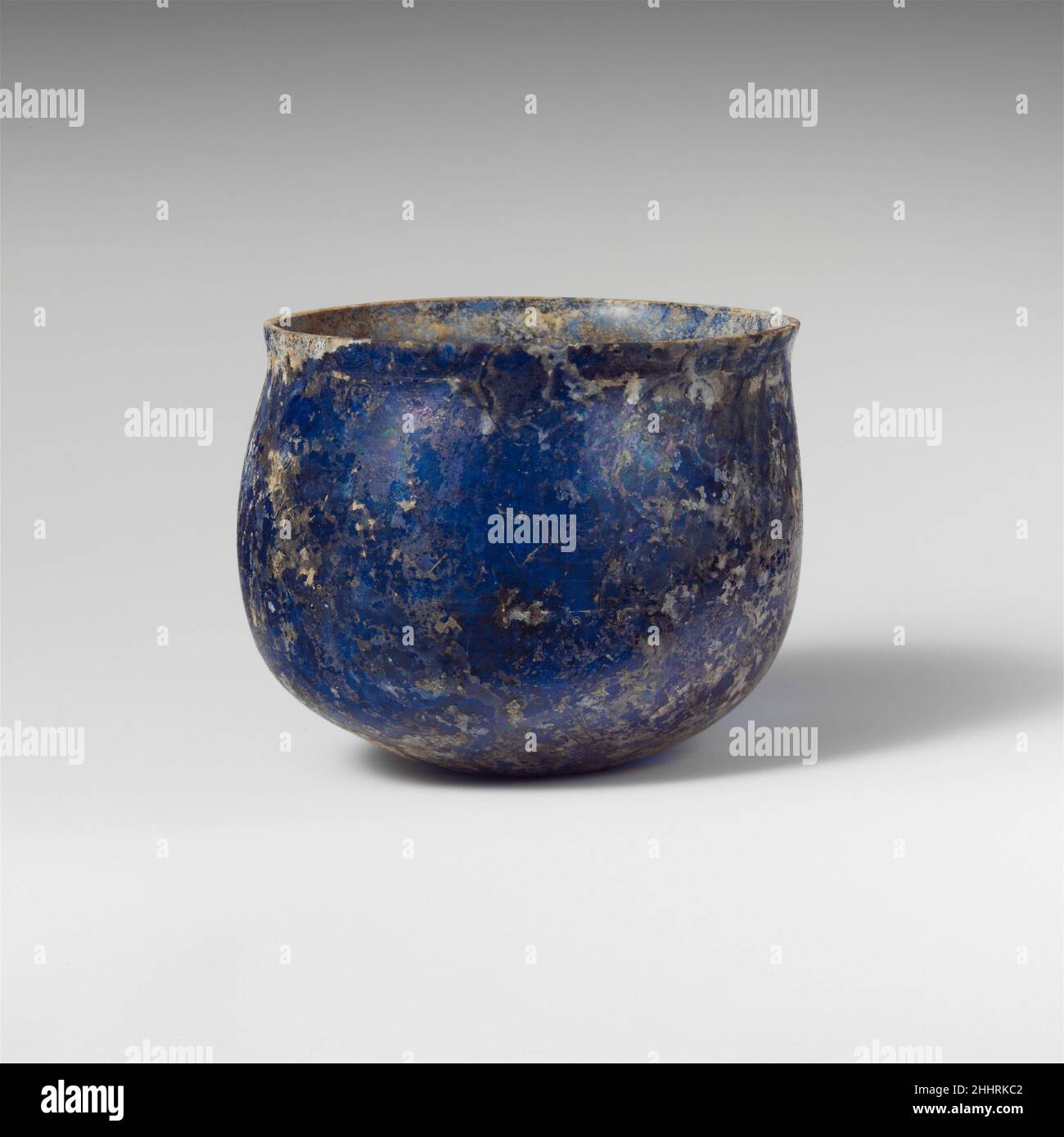 Glasbecher 1st. Jahrhundert n. Chr. römisch Durchscheinend blau.abgerissen, horizontaler Rand, mit leichter Wölbung unten; uneben, konvexe Seite zum Körper; abgerundeter Boden, mit kleinem konkaven Zentrum.schwache, am Rad abrassige horizontale Linien, eine 0,4 cm unter dem Rand, zwei weitere am Körper an der Spitze des größten Durchmessers.gebrochen und repariert; wenige Blasen; Stumm und weißlich, schillernde Verwitterung, die viel von Oberflächen bedeckt. Glasbecher 244584 Stockfoto