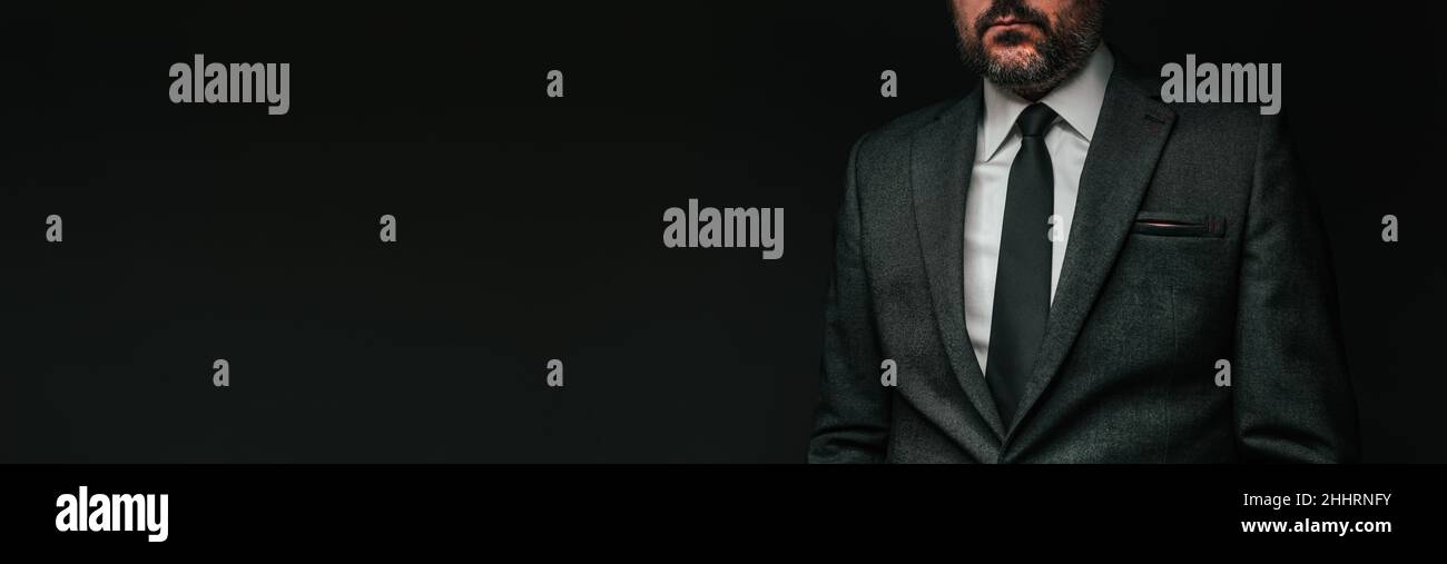 Panorama-Porträt eines gutaussehenden, selbstbewussten Geschäftsmannes in elegantem grauen Anzug vor dunklem Hintergrund Stockfoto