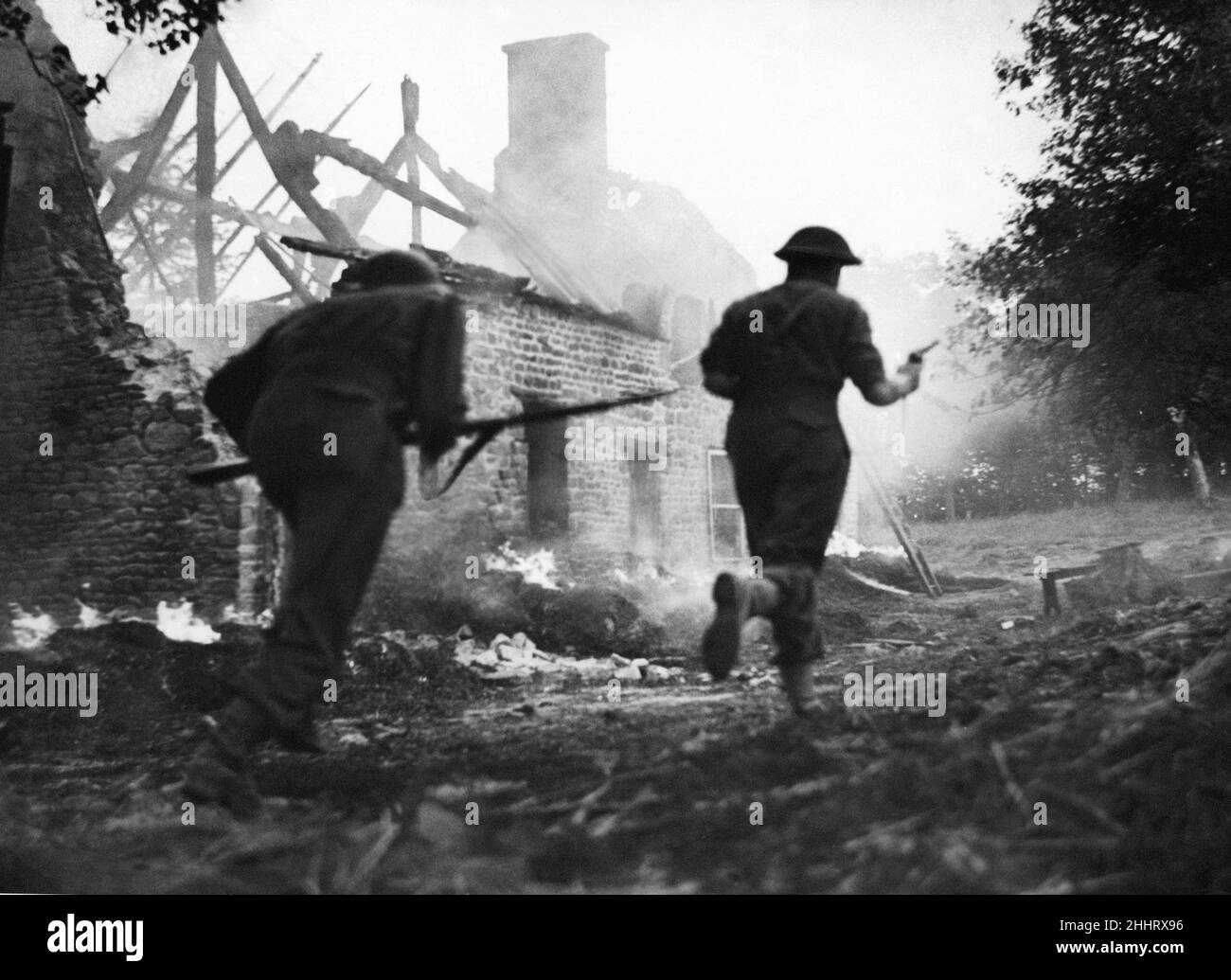Der Vormarsch südlich von Le Beny Bocage geht weiter. Britische Infanterie ist hier zu sehen, wie sie an den brennenden Resten eines Bauernhauses vorbeirast, um dem Feind zu folgen. Die Deutschen hatten die Gebäude als Quartier genutzt. August 1944 Stockfoto