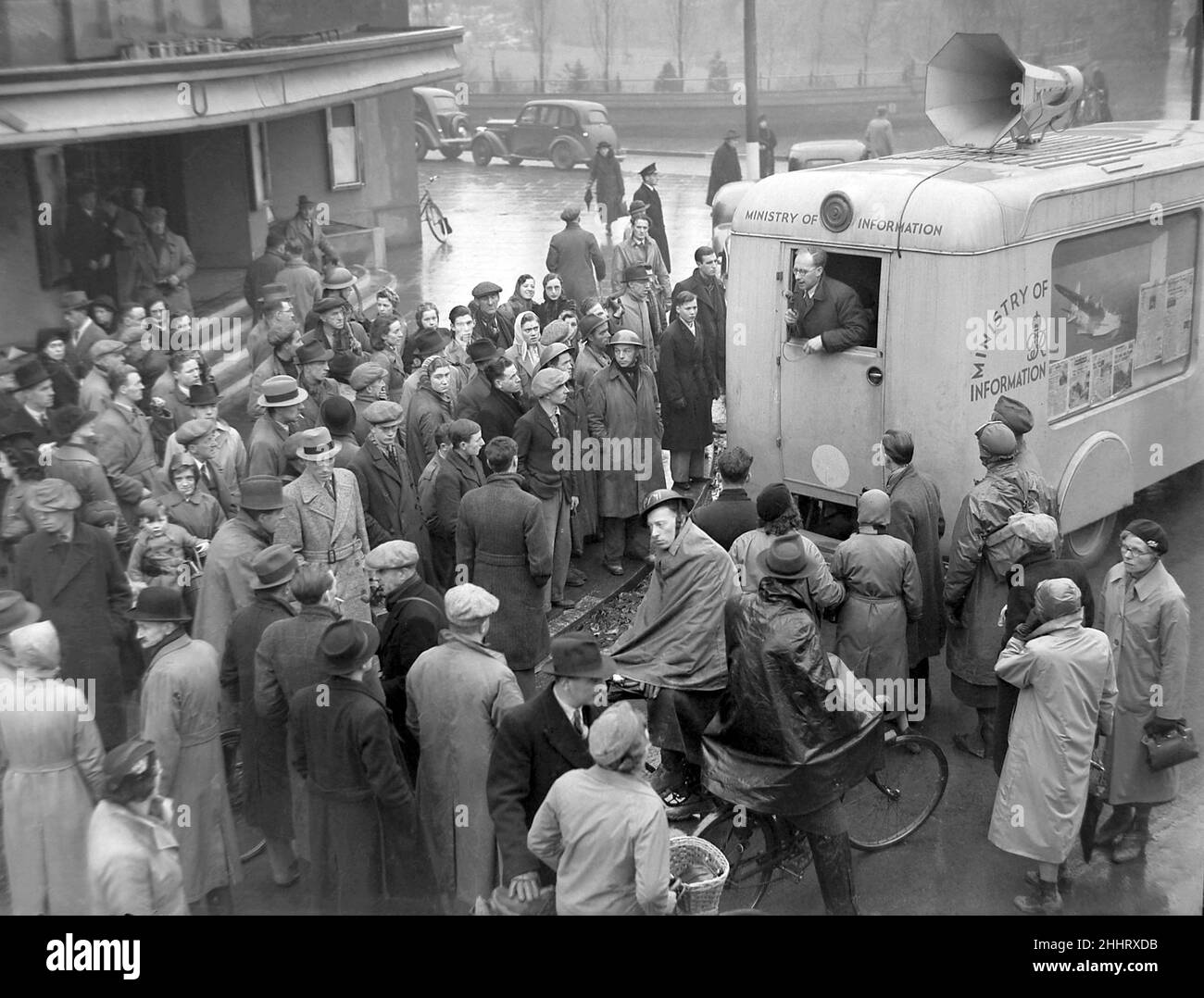 Menschen versammeln sich um den Transporter des Informationsministeriums, der vor dem Coventry Hippodrome Theatre in der Hales Street geparkt ist, um Ansagen und Ratschläge über ein lautes Lautsprechersystem und ein Mikrofon zu hören. In der Ferne ist der Garten von Lady Herbert zu sehen. 18th. November 1940 Stockfoto