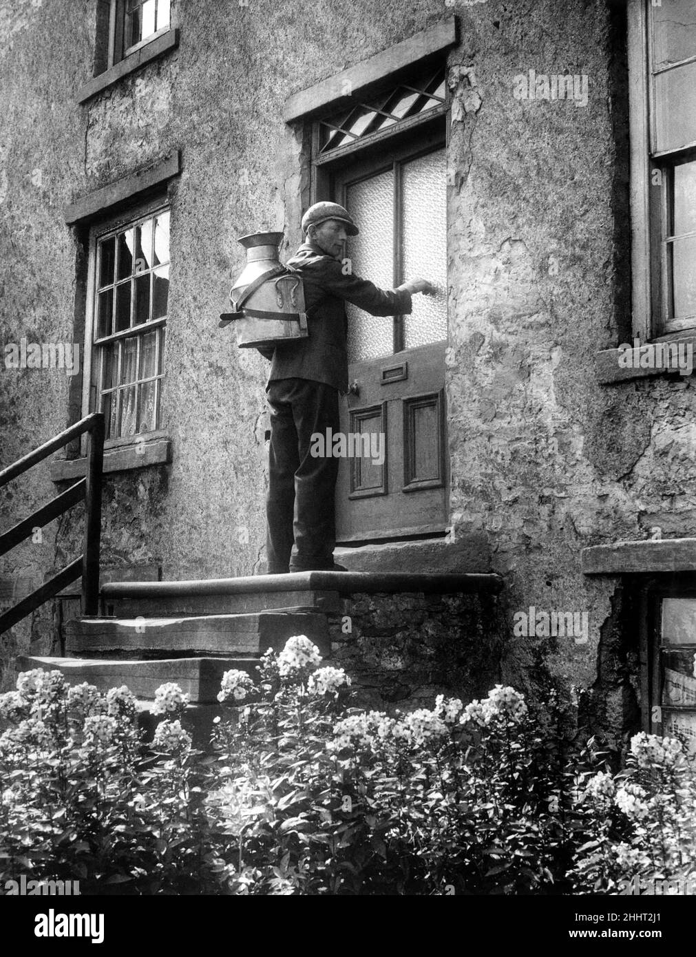 Der Dorfmilchmann George Wake macht seine täglichen Runden in den Yorkshire Dales mit seiner viereinhalb Gallonen großen Milchkanne, die ihm auf den Rücken geschnallt wird. 8th. August 1944. Stockfoto